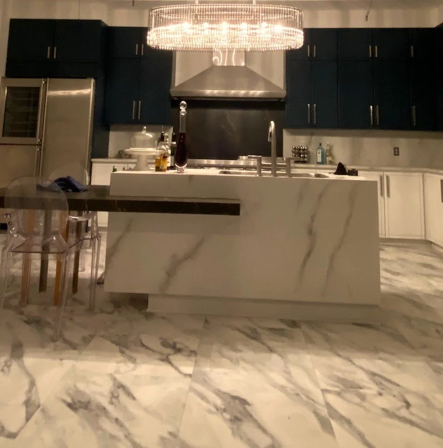 Kitchen set with a white marble-look waterfall island and marble floor tiles under a crystal chandelier, studio rigging overhead