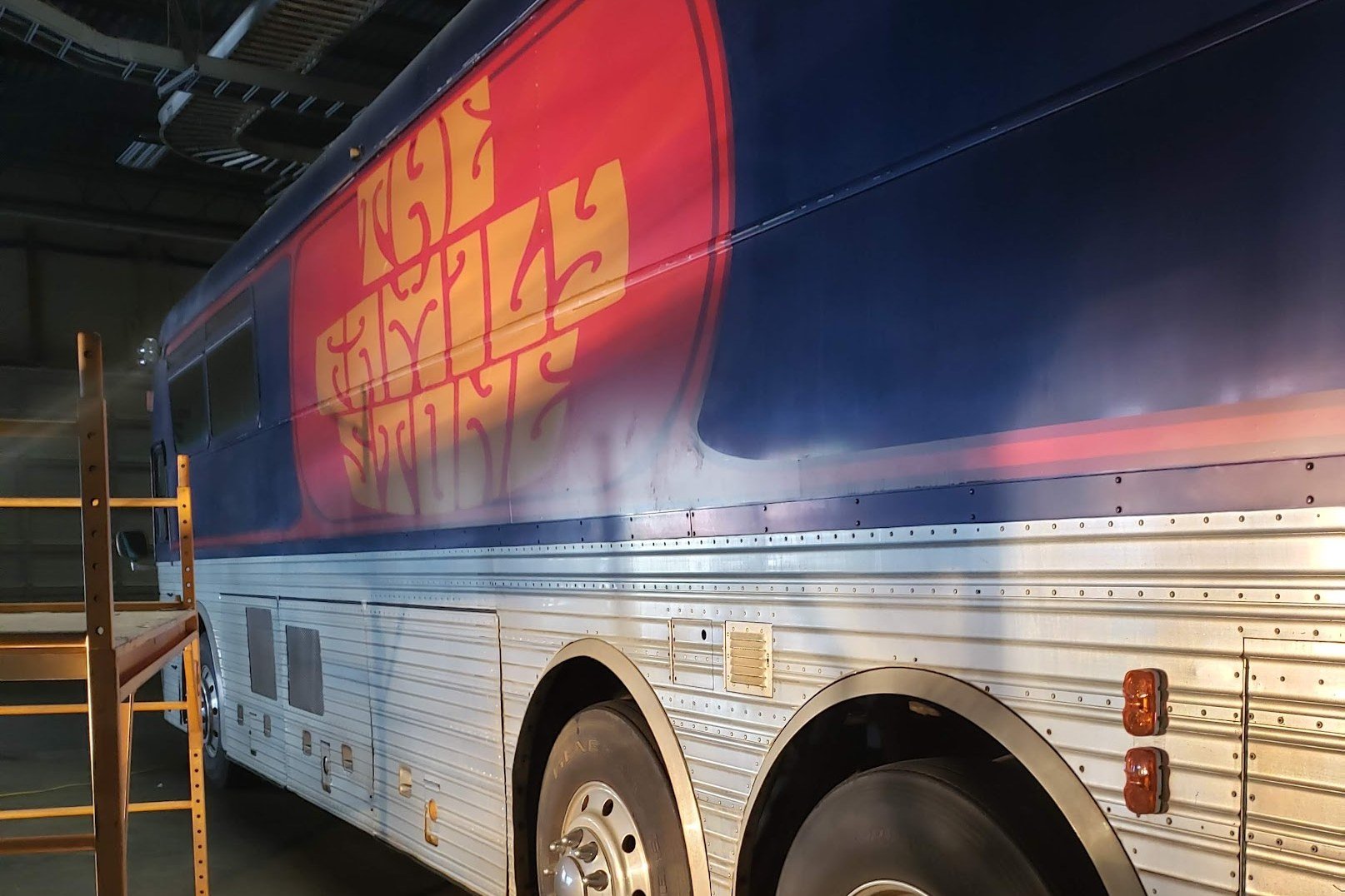 Full-size bus covered in a full vinyl wrap with a bold red and blue graphic, parked indoors