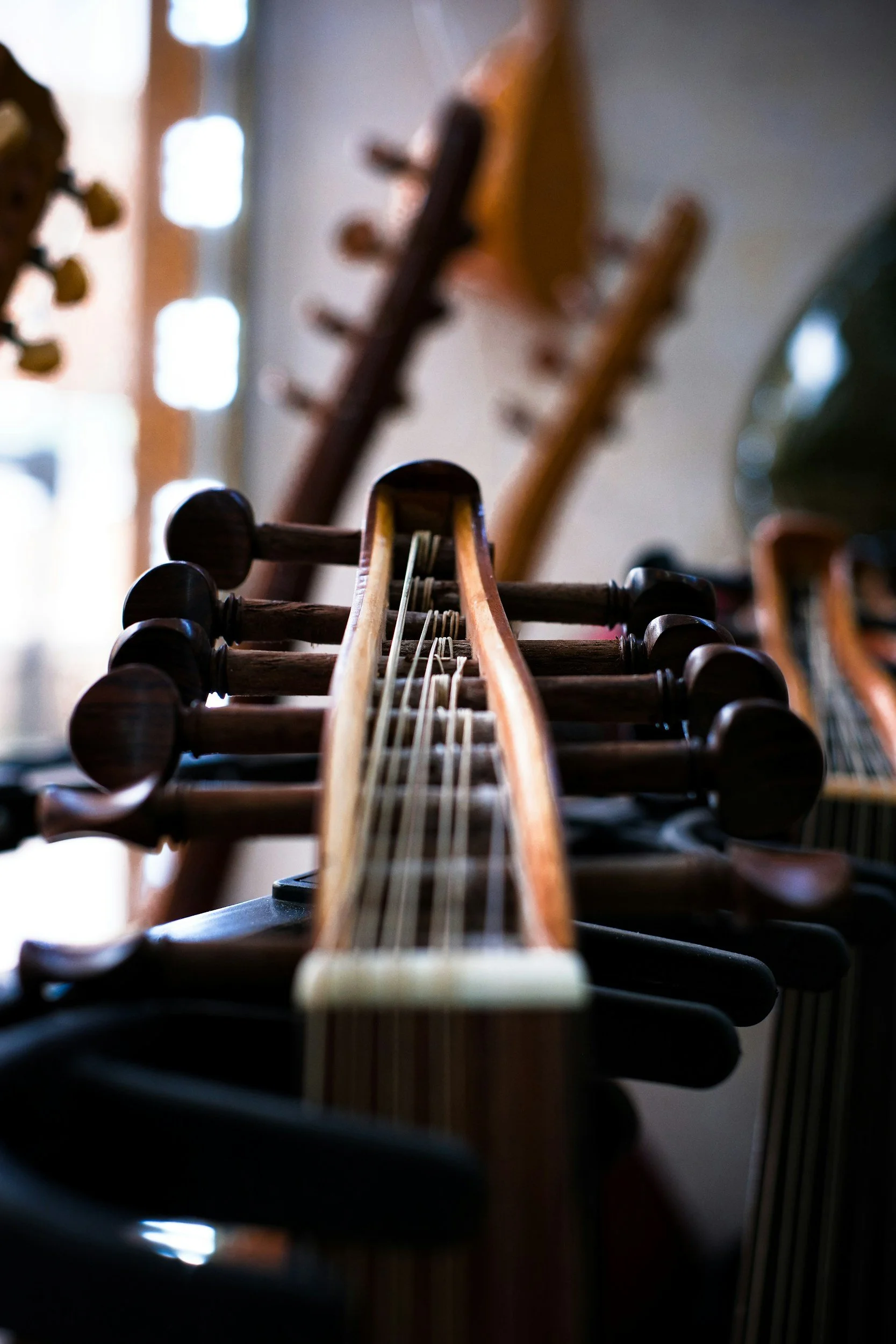 Close-up of the fretboard and headstock of a classical guitar, with a blurred background showing guitars hanging on the wall.
