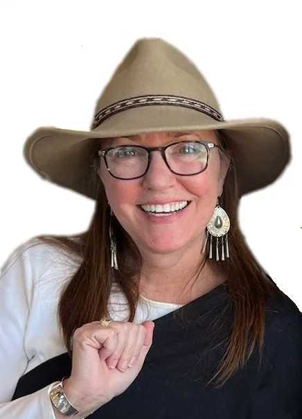 Woman wearing a wide-brimmed hat and glasses, smiling, with earrings and a white shirt.