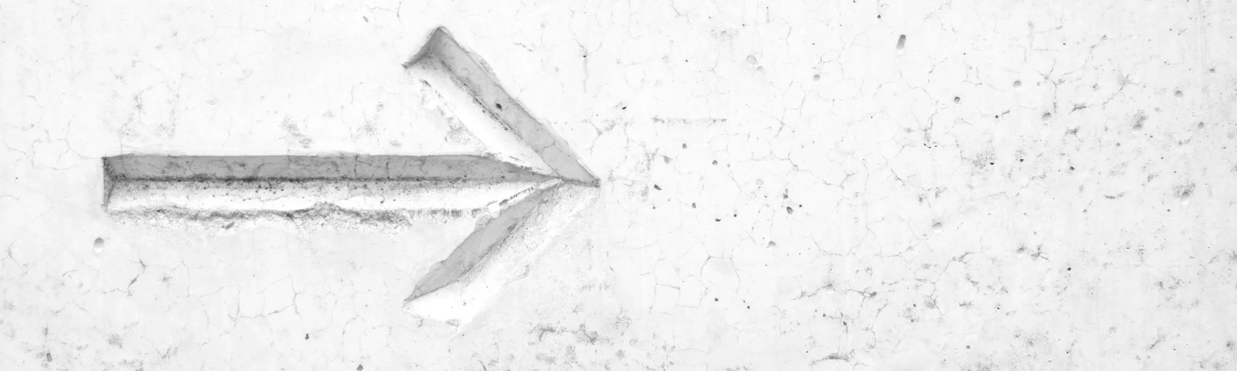 A white wall with a textured, cracked surface and a carved arrow pointing to the right.