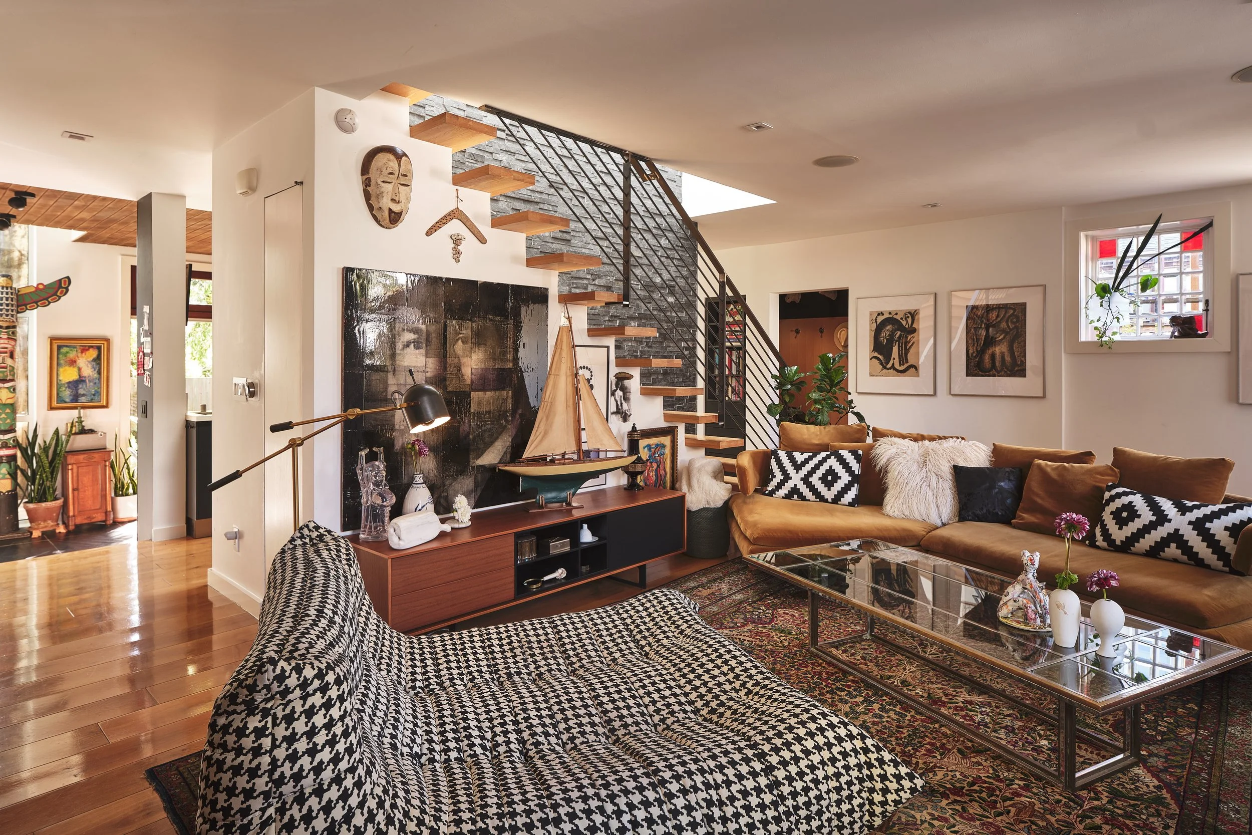 A spacious living room with a sectional sofa, patterned pillows, artwork on the walls, a glass coffee table, and decorative items, including a model sailboat, on a wooden console.