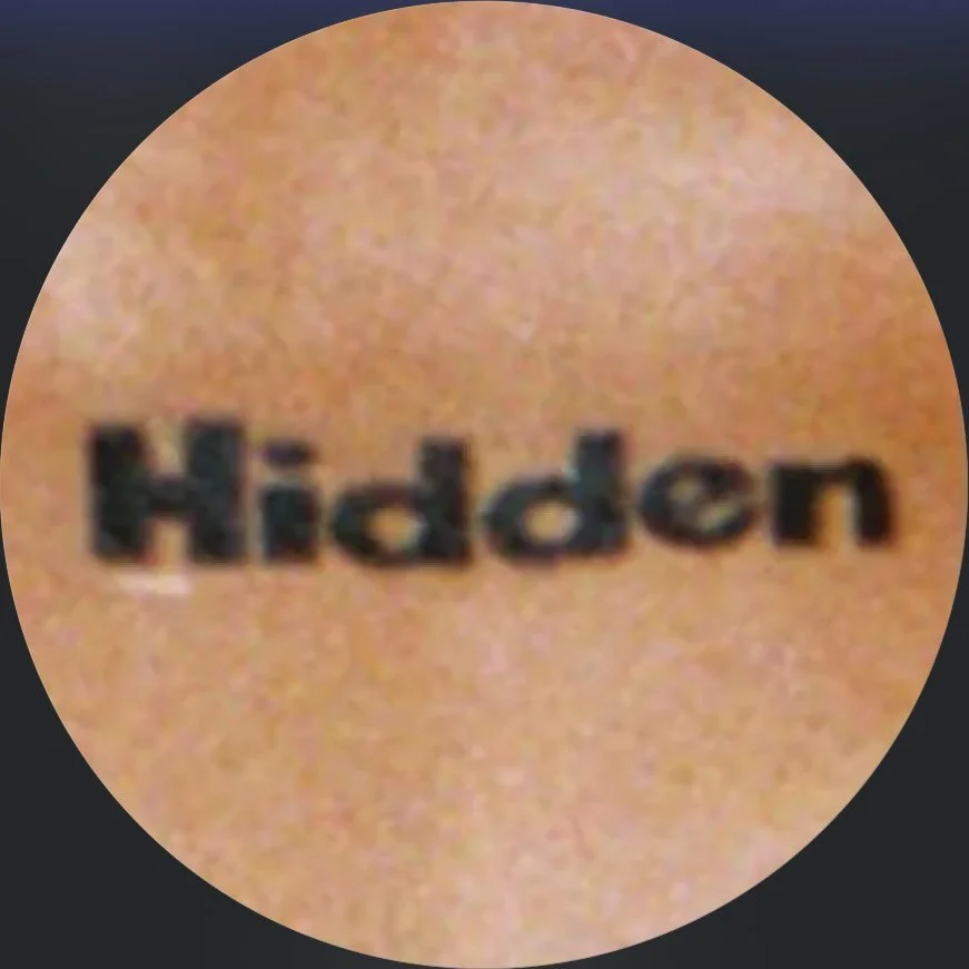 Close-up of the word 'Hidden' printed on a person's skin, possibly as a tattoo or inked text.
