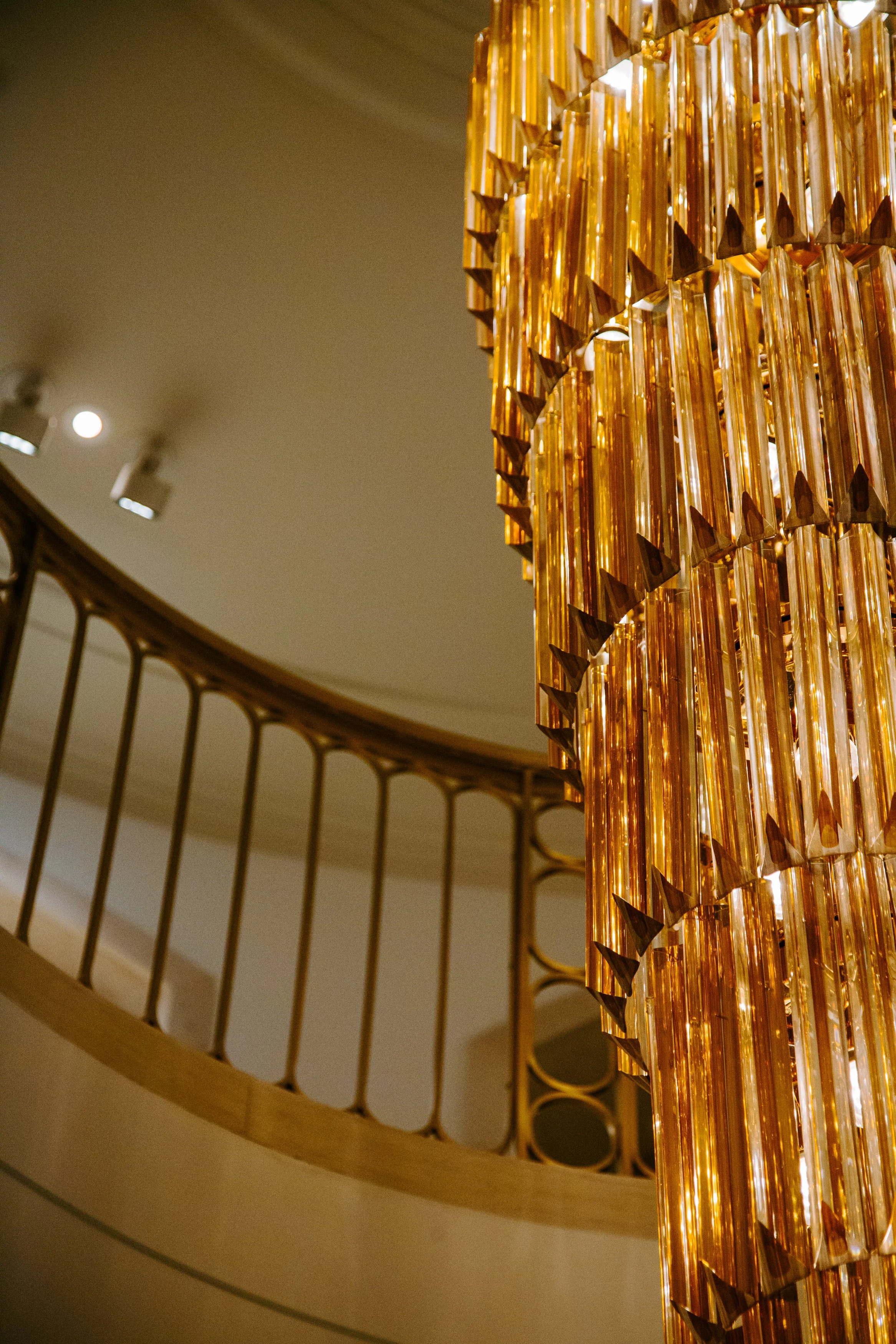 Close-up of a luxurious gold chandelier hanging in a building with curved ceilings and a decorative railing.