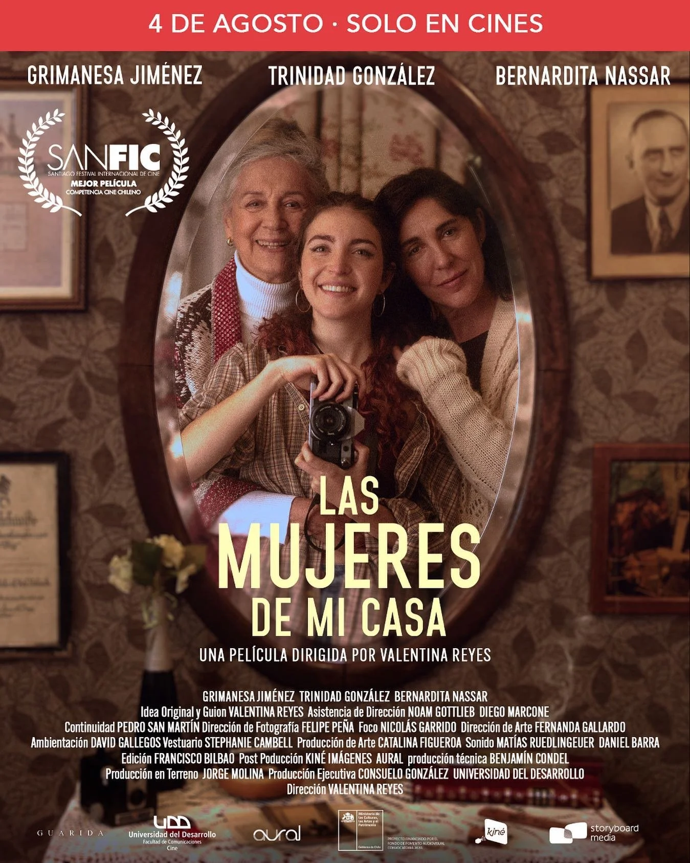 Cartel promocional de la película "Las Mujeres de Mi Casa" que se estrena el 4 de agosto en cines, con una foto de tres mujeres sonriendo en un espejo, con cuadros en la pared y un florero con flores en primer plano.