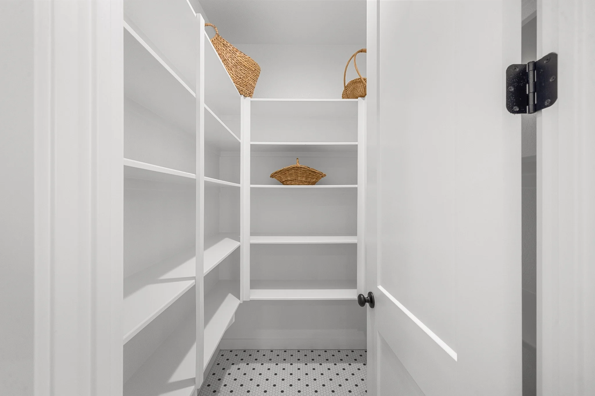 Interior of a white walk-in pantry with an open door, featuring multiple empty shelves on both sides and a small basket on the top shelf inside.