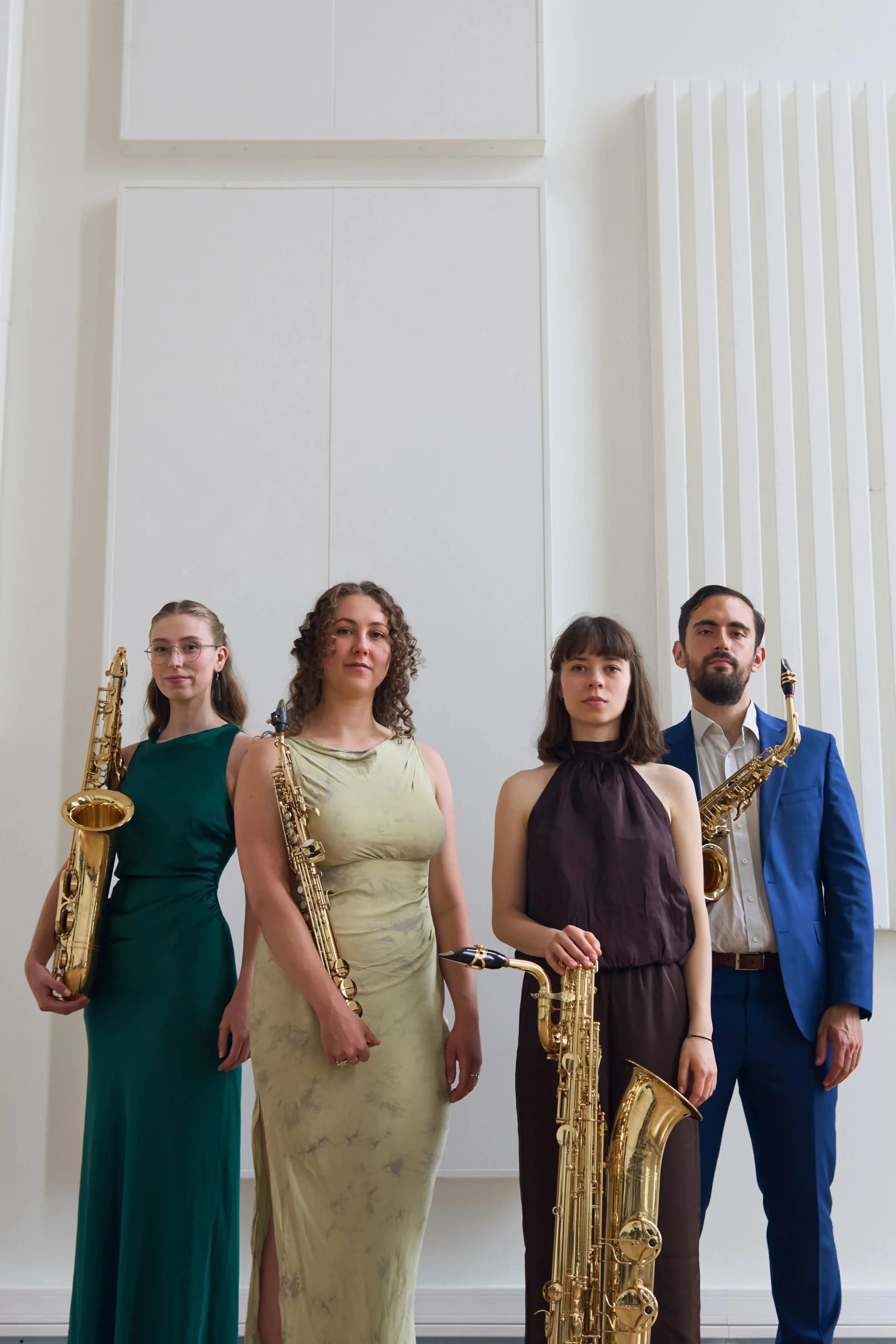 Group of four musicians in formal attire holding saxophones standing in a white room.