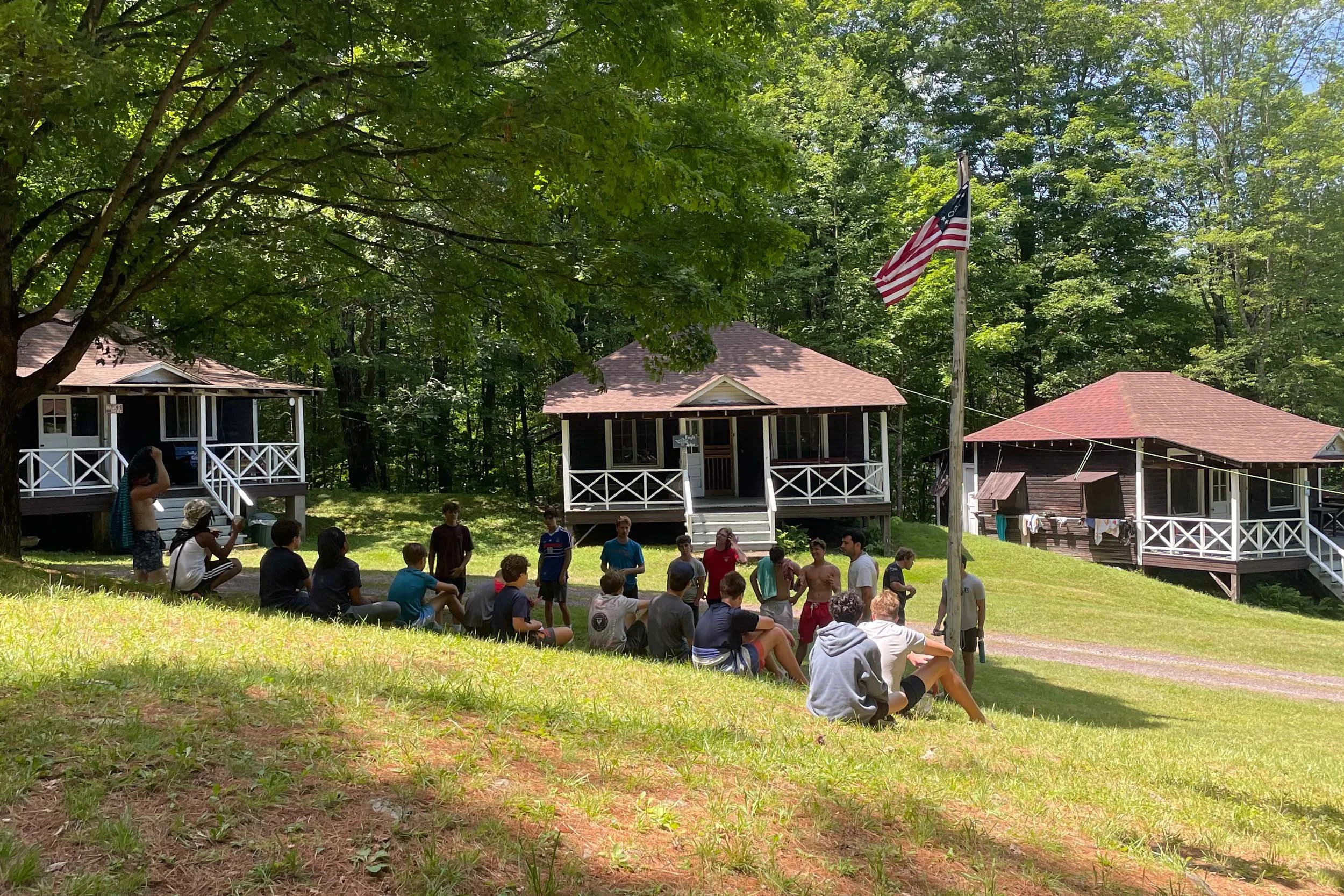 Campers and staff gathered around the flagpole with a line of cabins behind them.