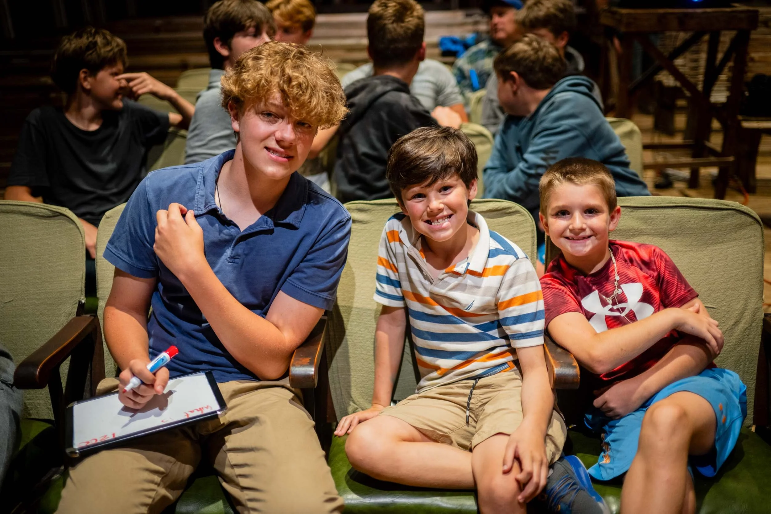 Two boys sitting next to their counselor working together during trivia night.