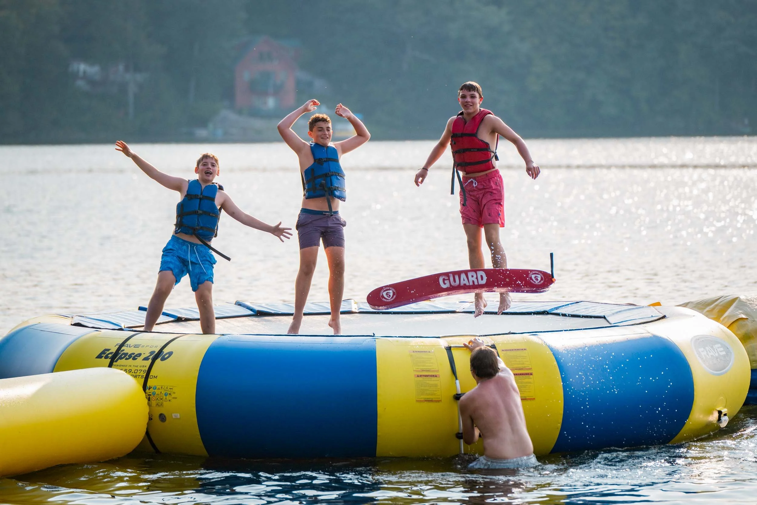 Three boys jumping on an inflatable water trampoline on the lake.