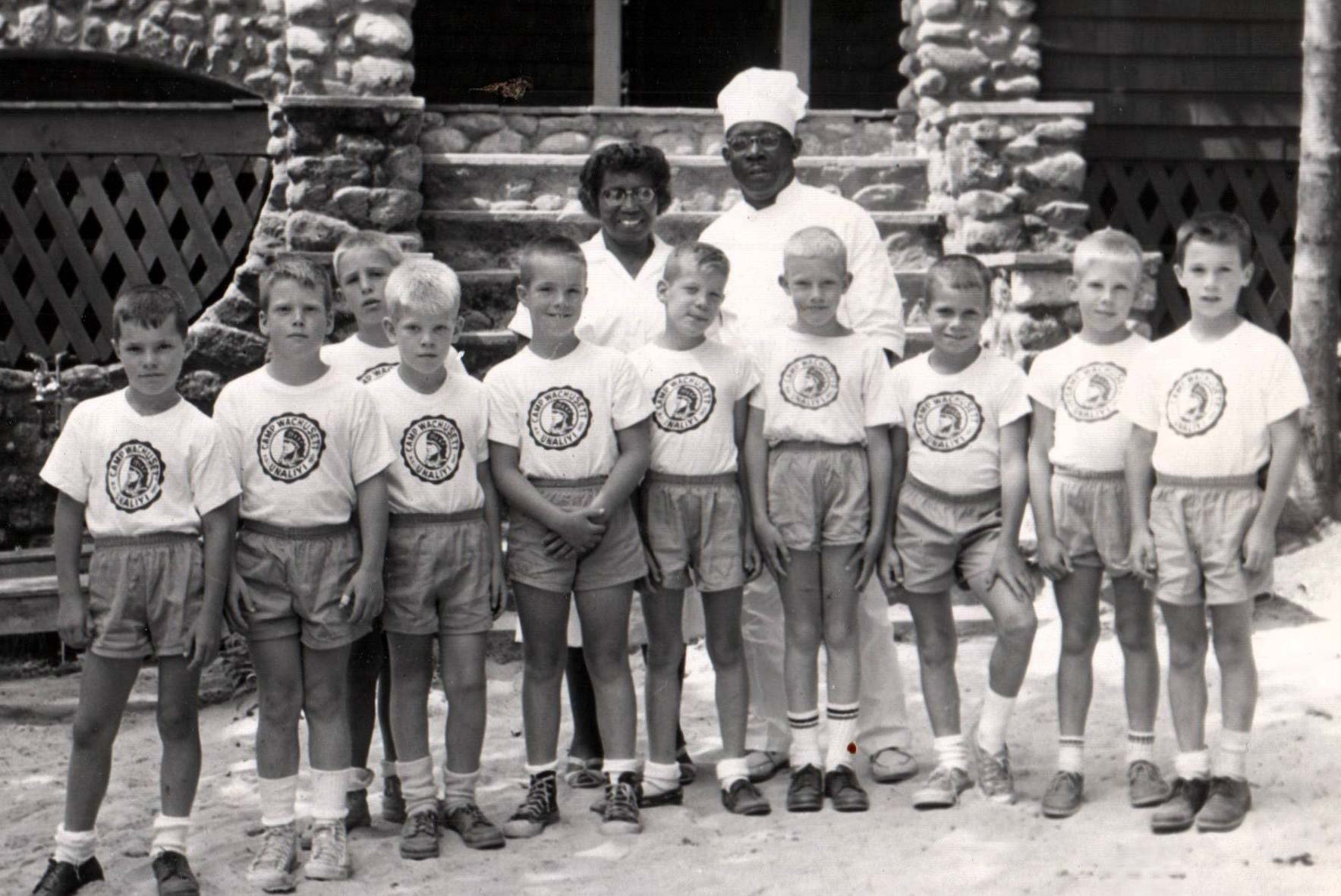 Black and white photo of a group of boys and two counselors in front of a stone staircase.