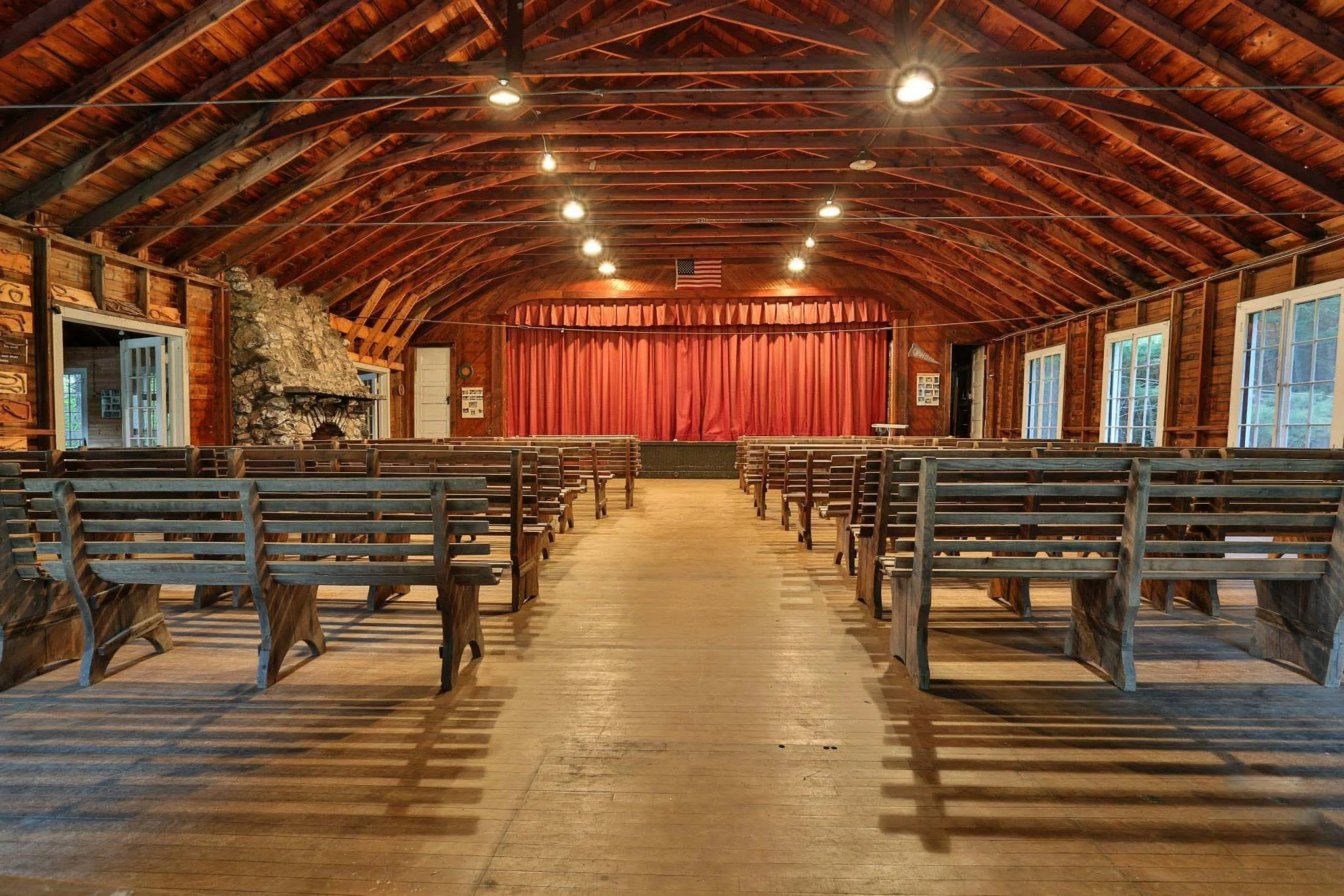A large wooden interior hall with a stage, benches, and fireplace.
