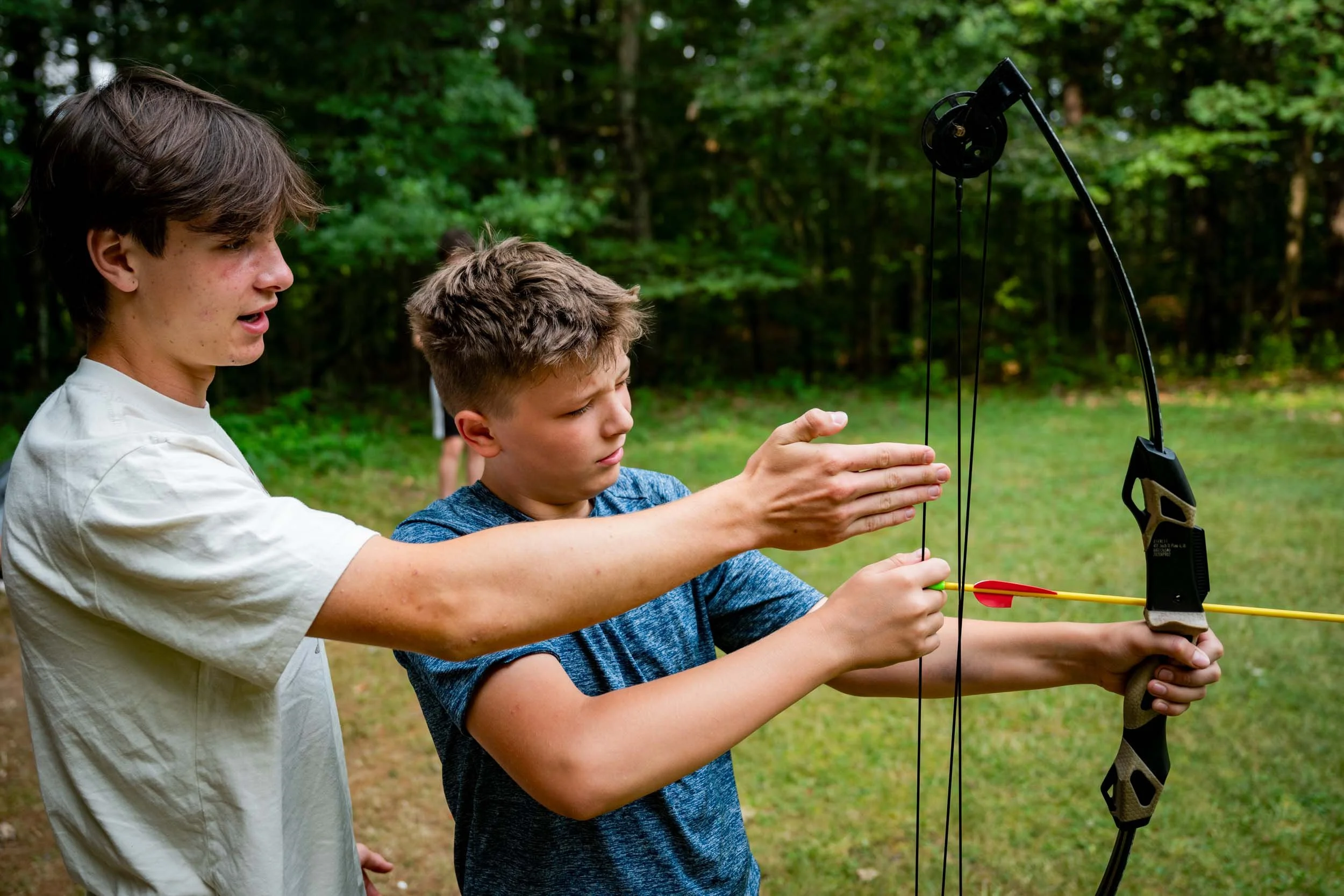 A counselor teaching a camper at the archery range.