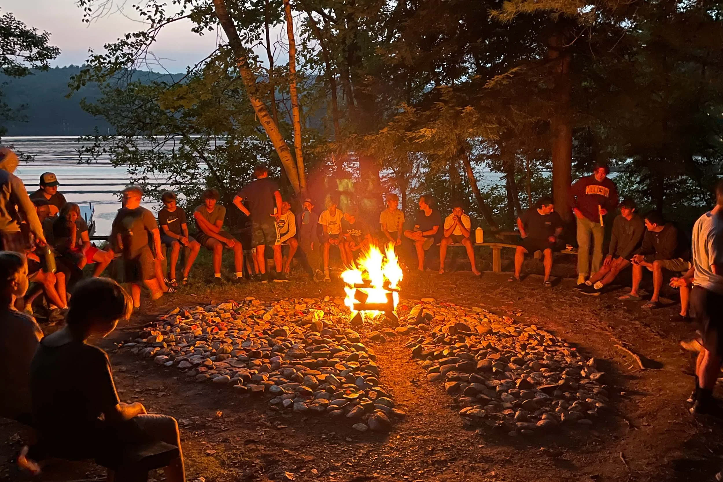 All of camp gathered outdoors around a campfire by the lakeside.