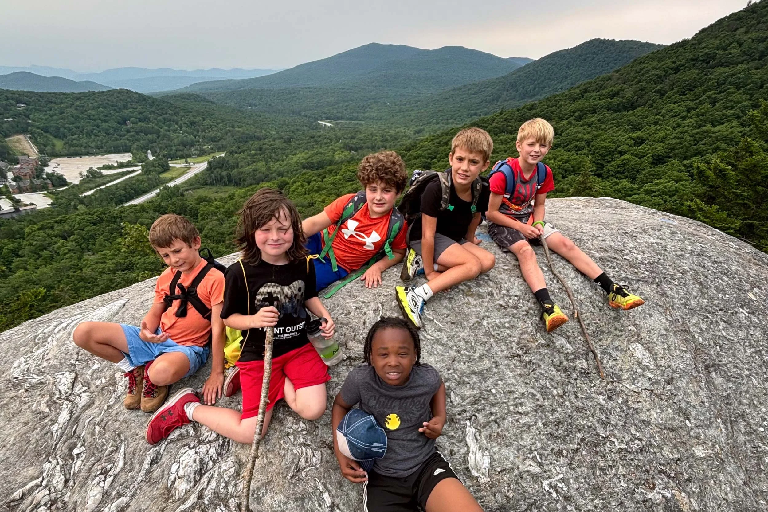 Young boys sitting and lying on a large rock summit with a scenic view behind them.