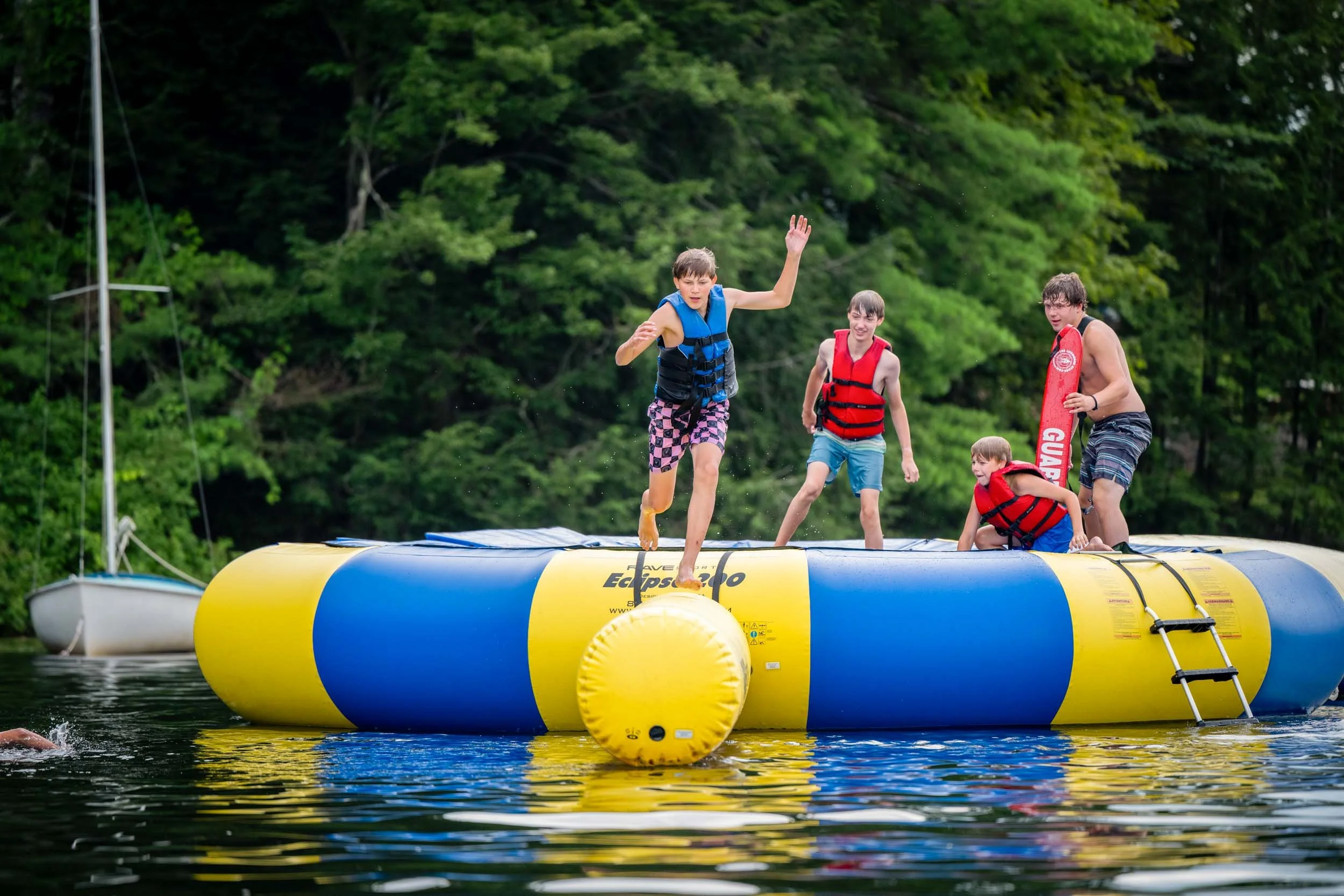 Campers playing on an inflatable water trampoline in a lake.