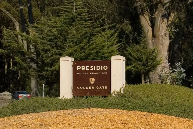 Sign for Presidio of San Francisco at the Golden Gate with trees in the background.