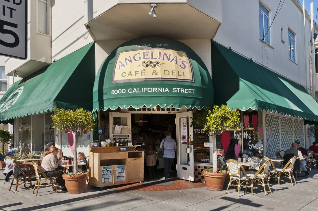 Exterior view of Angelina's Café & Deli at 6000 California Street, with outdoor seating, green awnings, potted plants, and customers dining outside.
