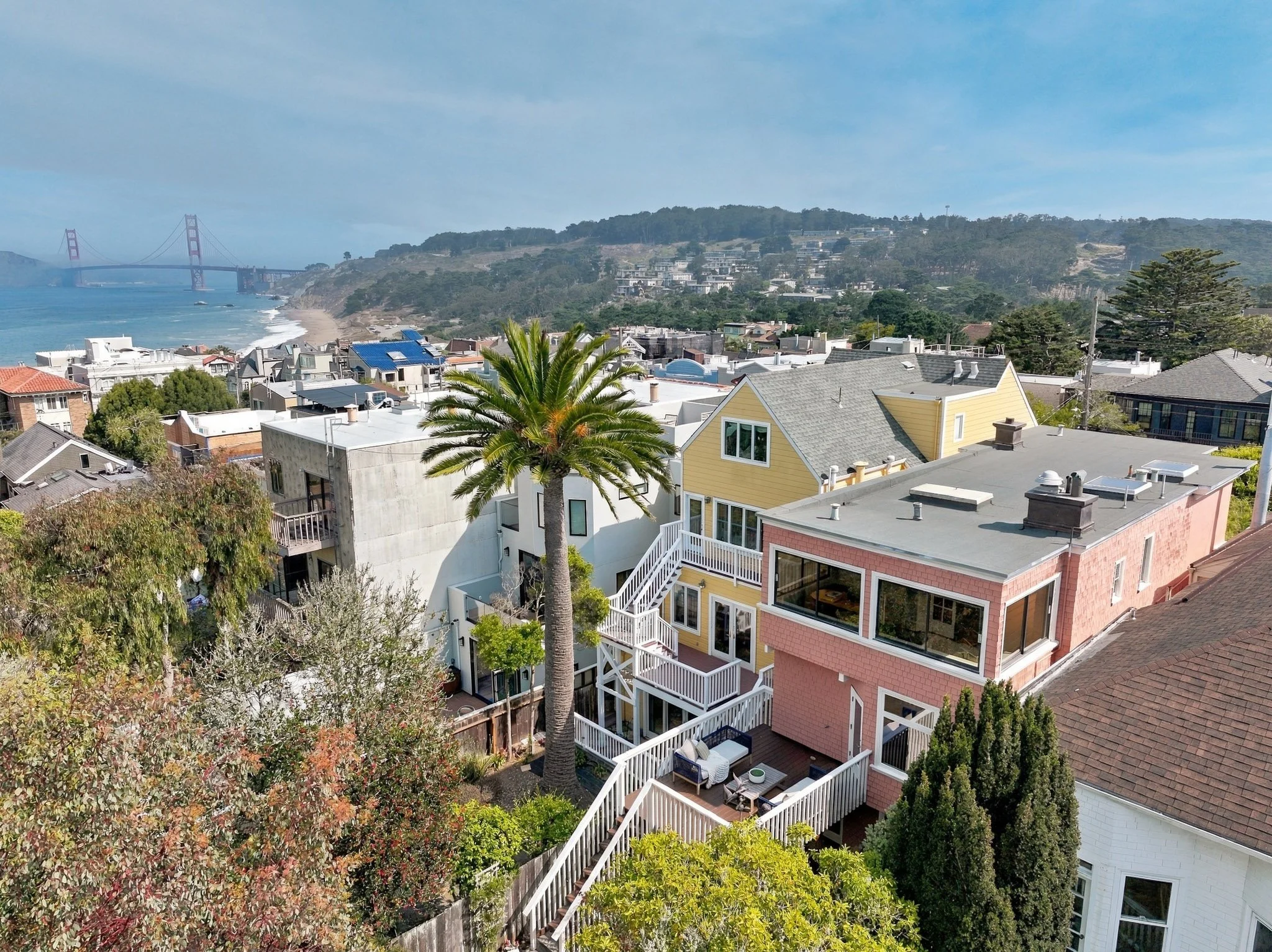 View of a beachfront neighborhood with houses, a palm tree, and a bridge in the background over the water