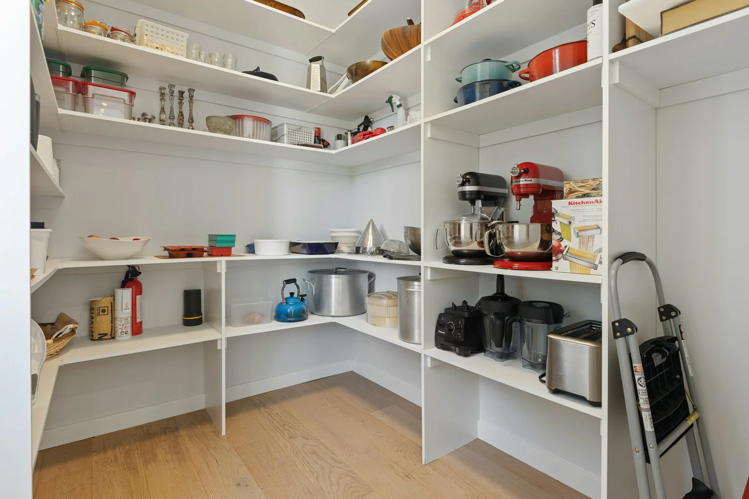 Walk-in pantry with white shelving for food, cookware, and small appliances