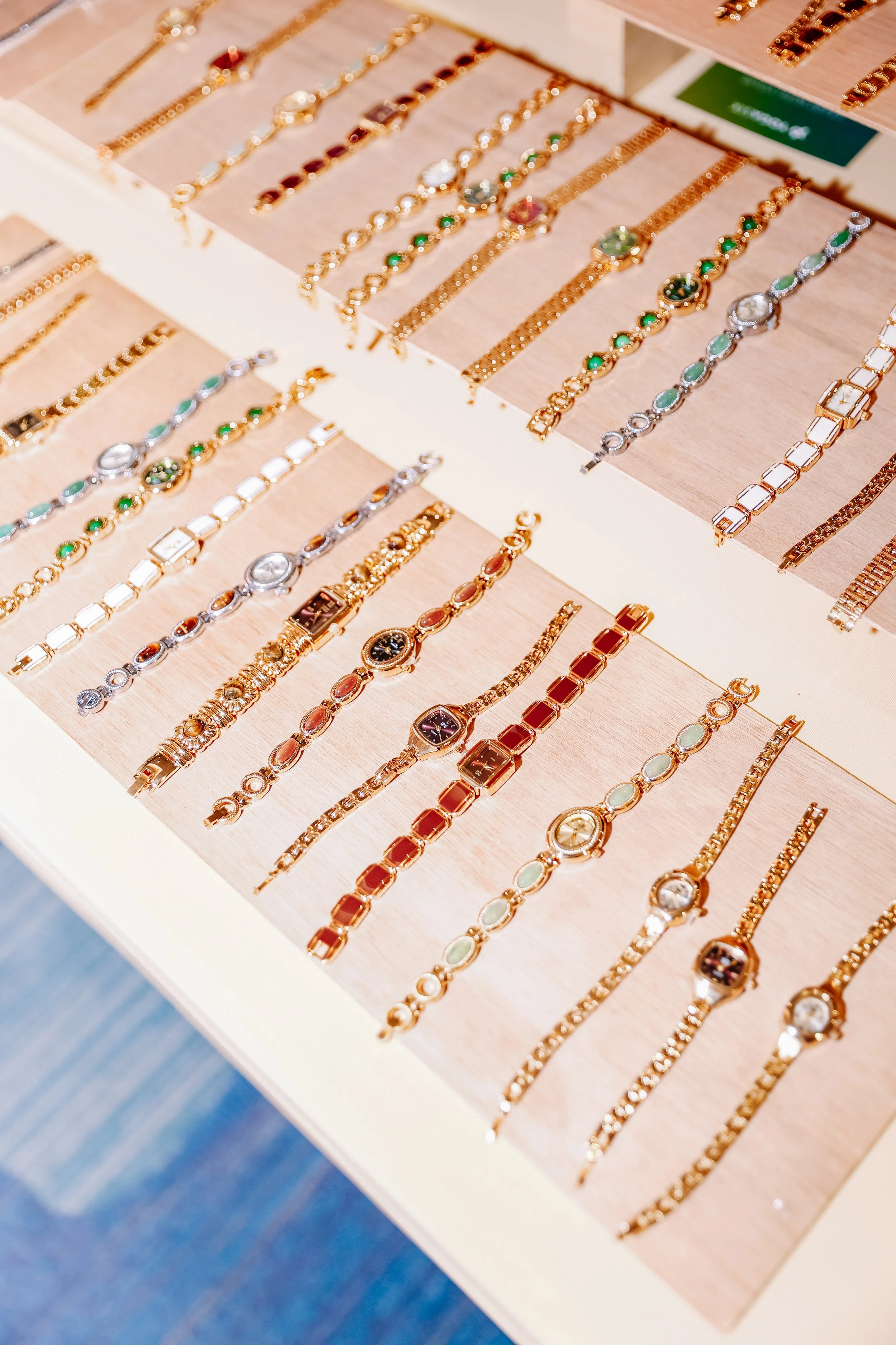 Display of various gold and silver watches and jewelry laid out on a light-colored surface in a jewelry store.