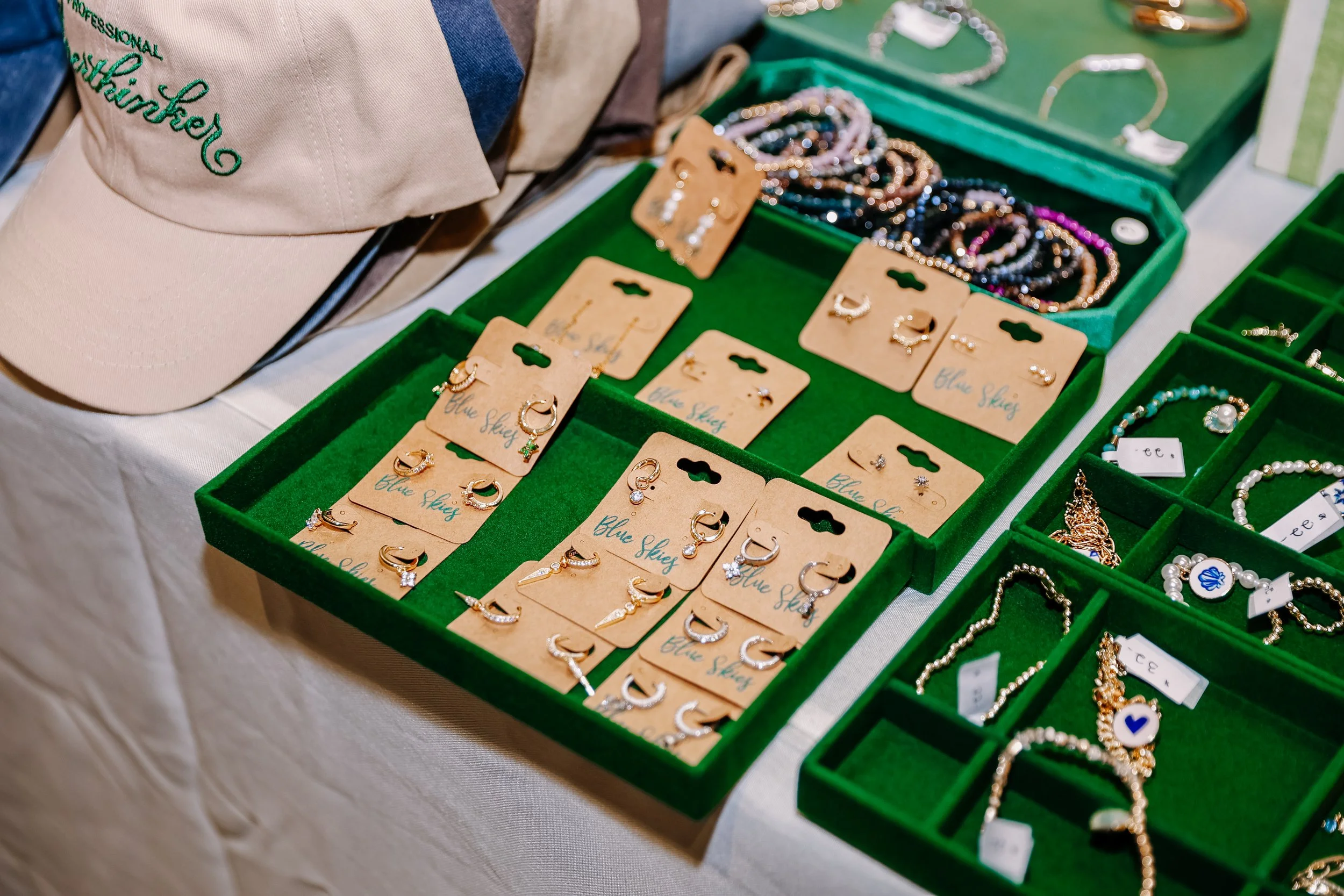 Display of jewelry including earrings, rings, bracelets, and necklaces in green velvet-lined boxes at a market stall.