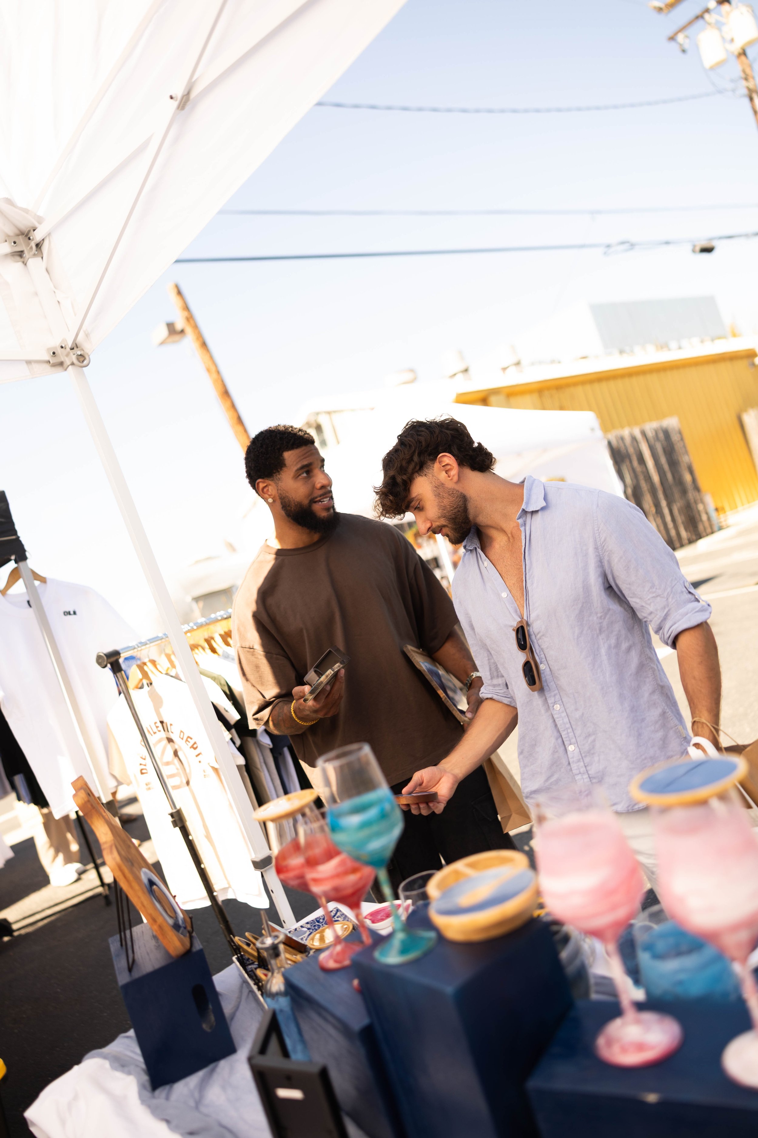Two men talking at an outdoor market stall with colorful ice cream desserts on display in the foreground.