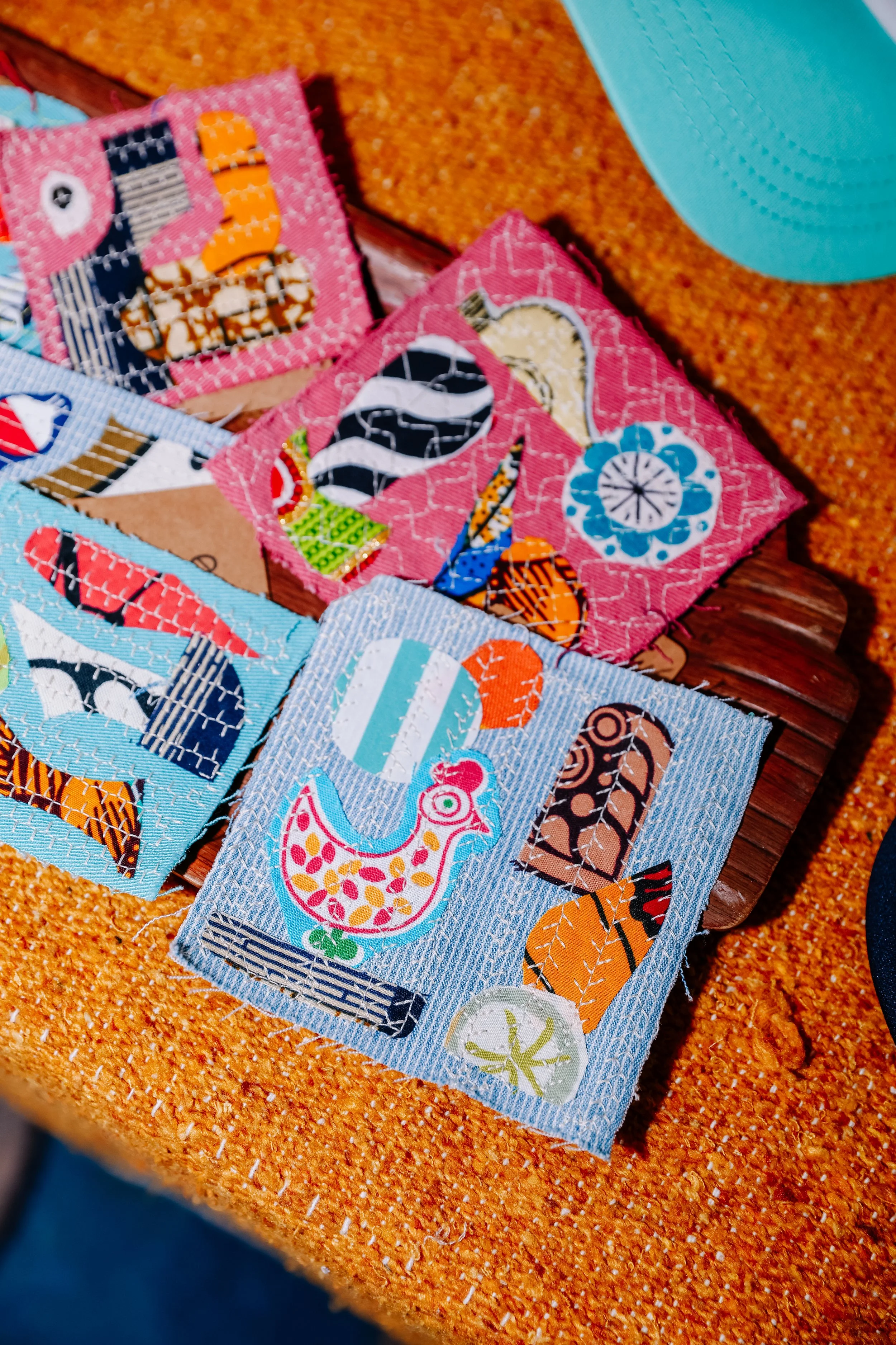 Colorful fabric squares with quilted patterns, including a chicken, a zebra, and flowers, arranged on a surface with orange, textured background.