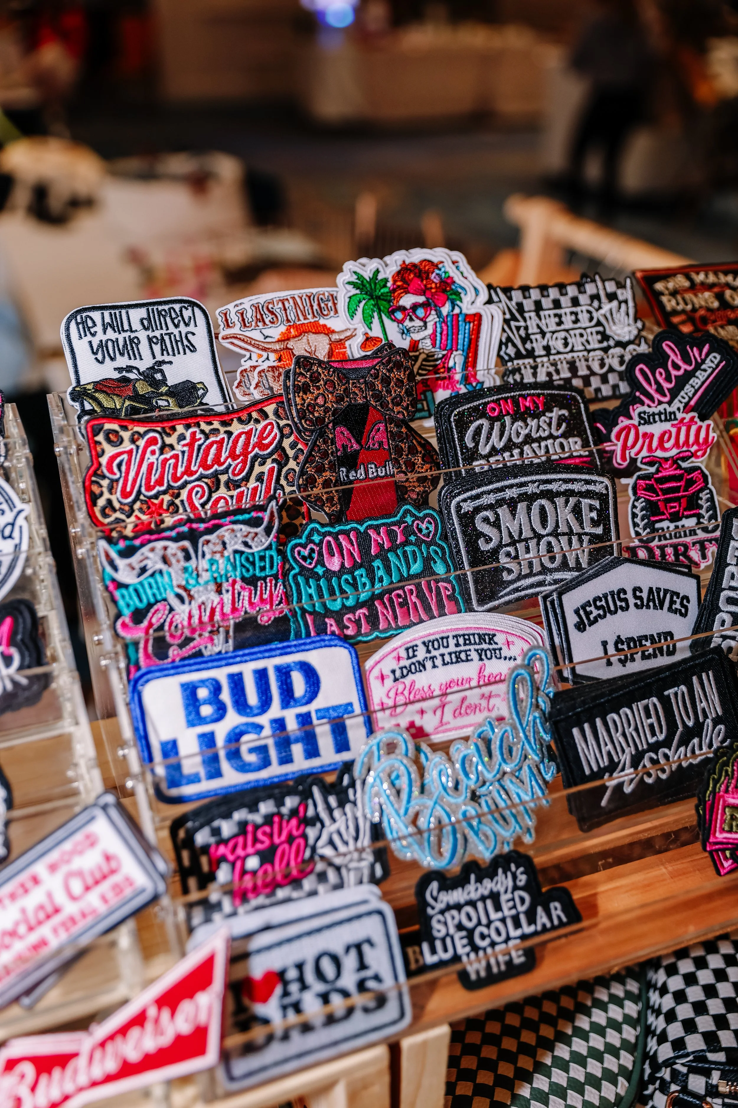 A display of colorful embroidered patches with various phrases and designs, including a leopard print bow, a Coca-Cola style logo, and humorous statements like 'He will direct your paths' and 'Last never.'