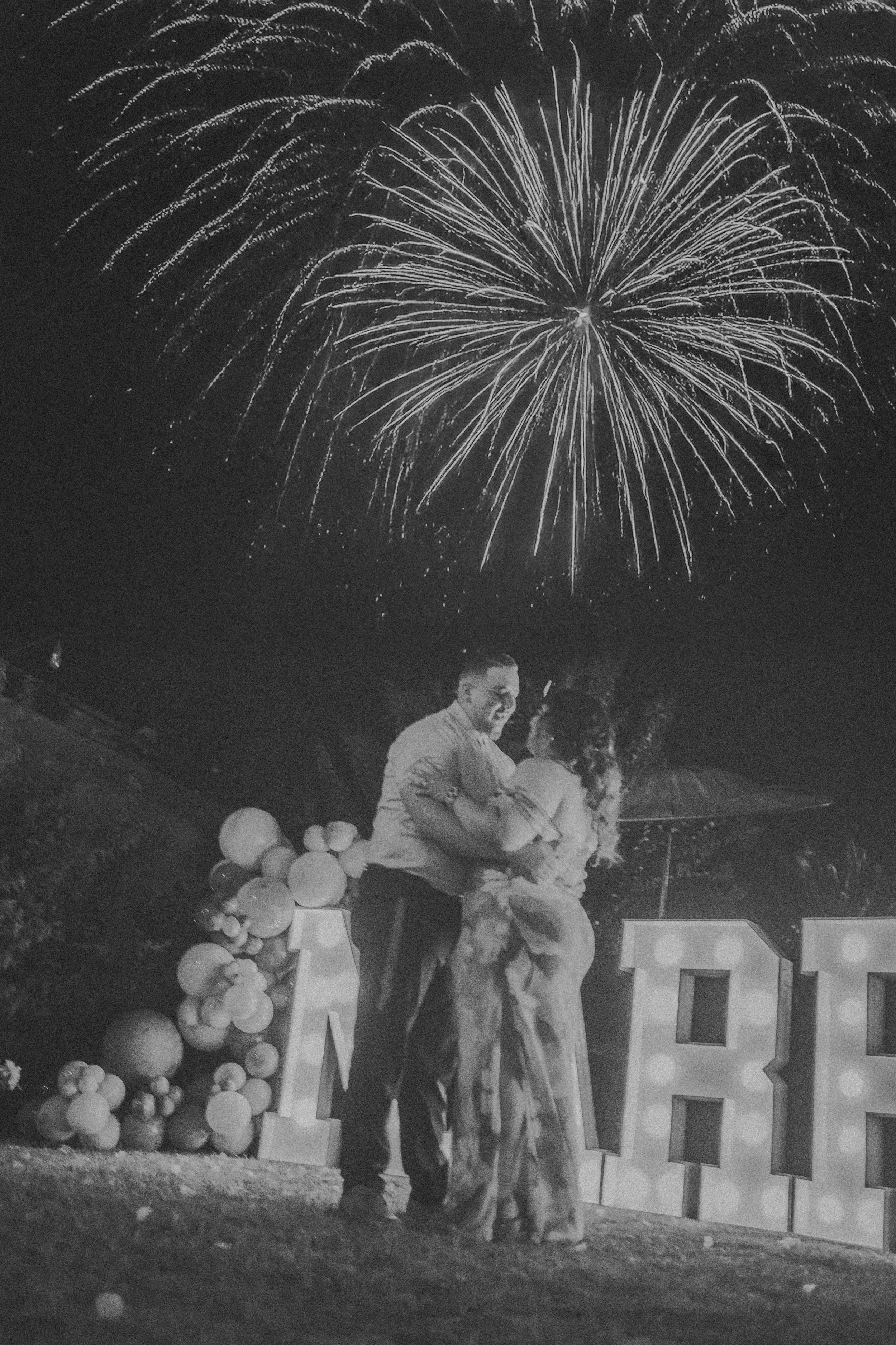 People celebrating outdoors with fireworks, balloons, and large illuminated letters spelling out 'APOLLO'.