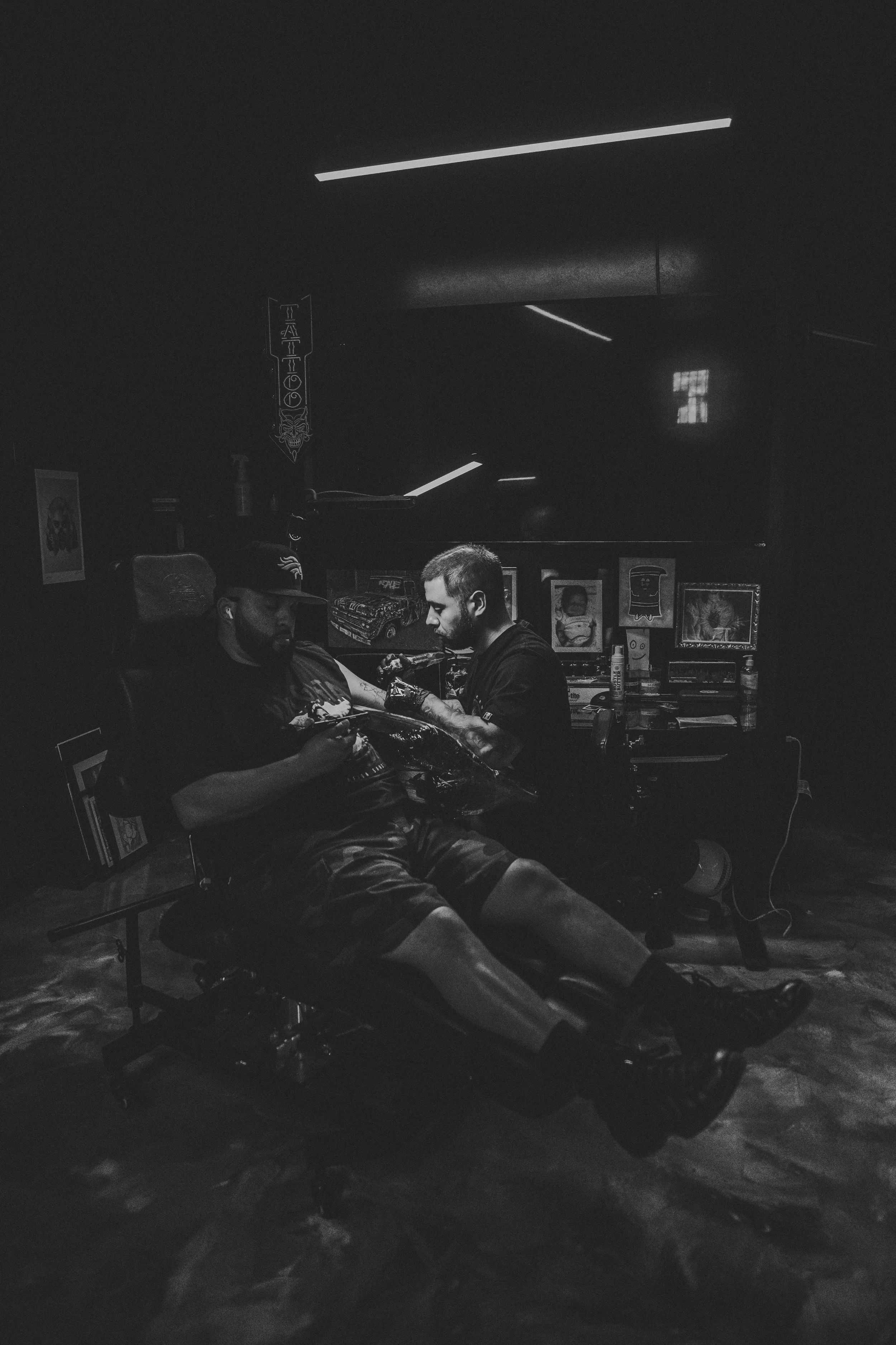 A person tattooing another person in a dimly lit room.