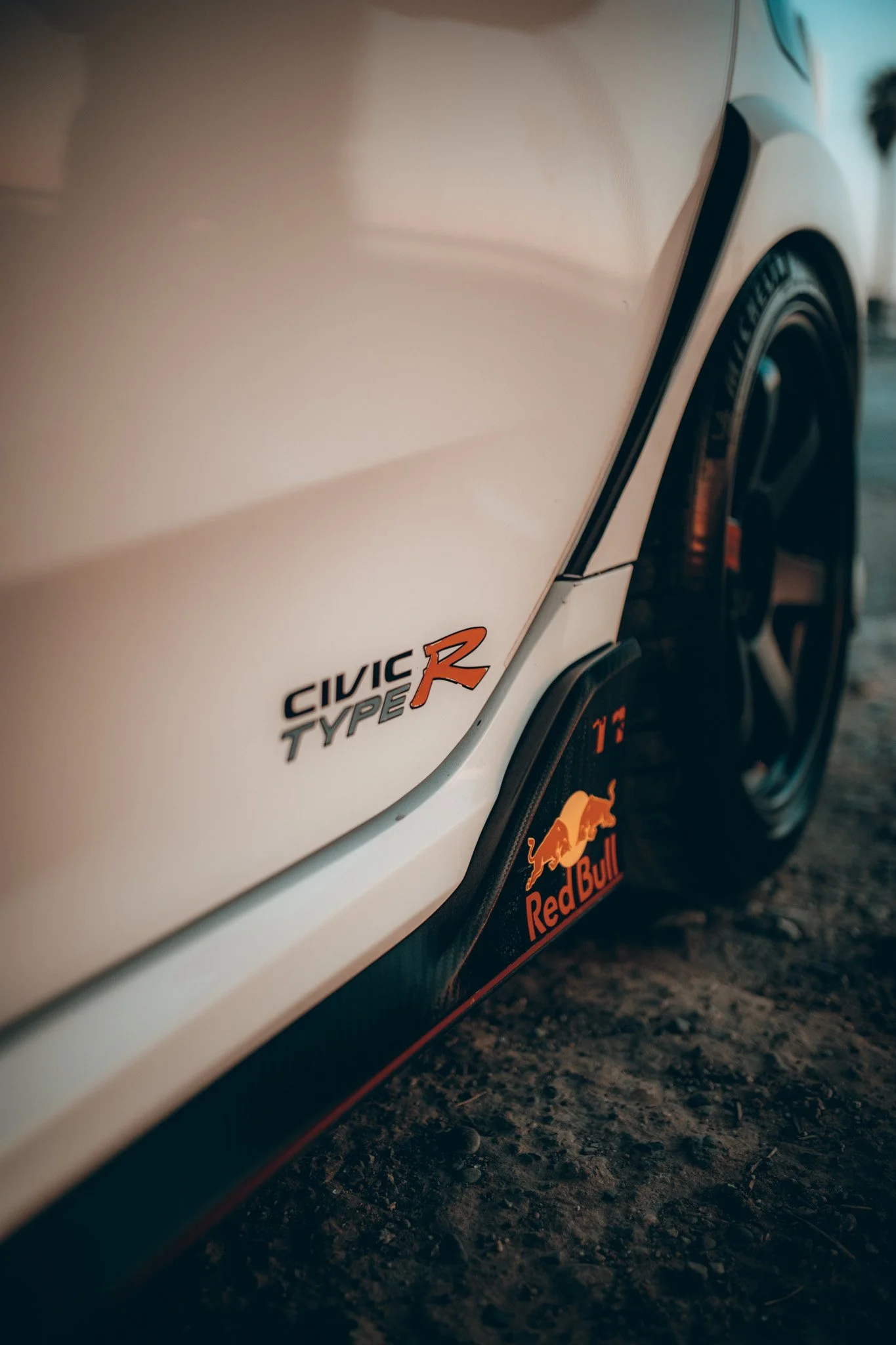 Close-up of a white Honda Civic Type R car with Red Bull logo on the mud flap, showing part of the front wheel and side panel.