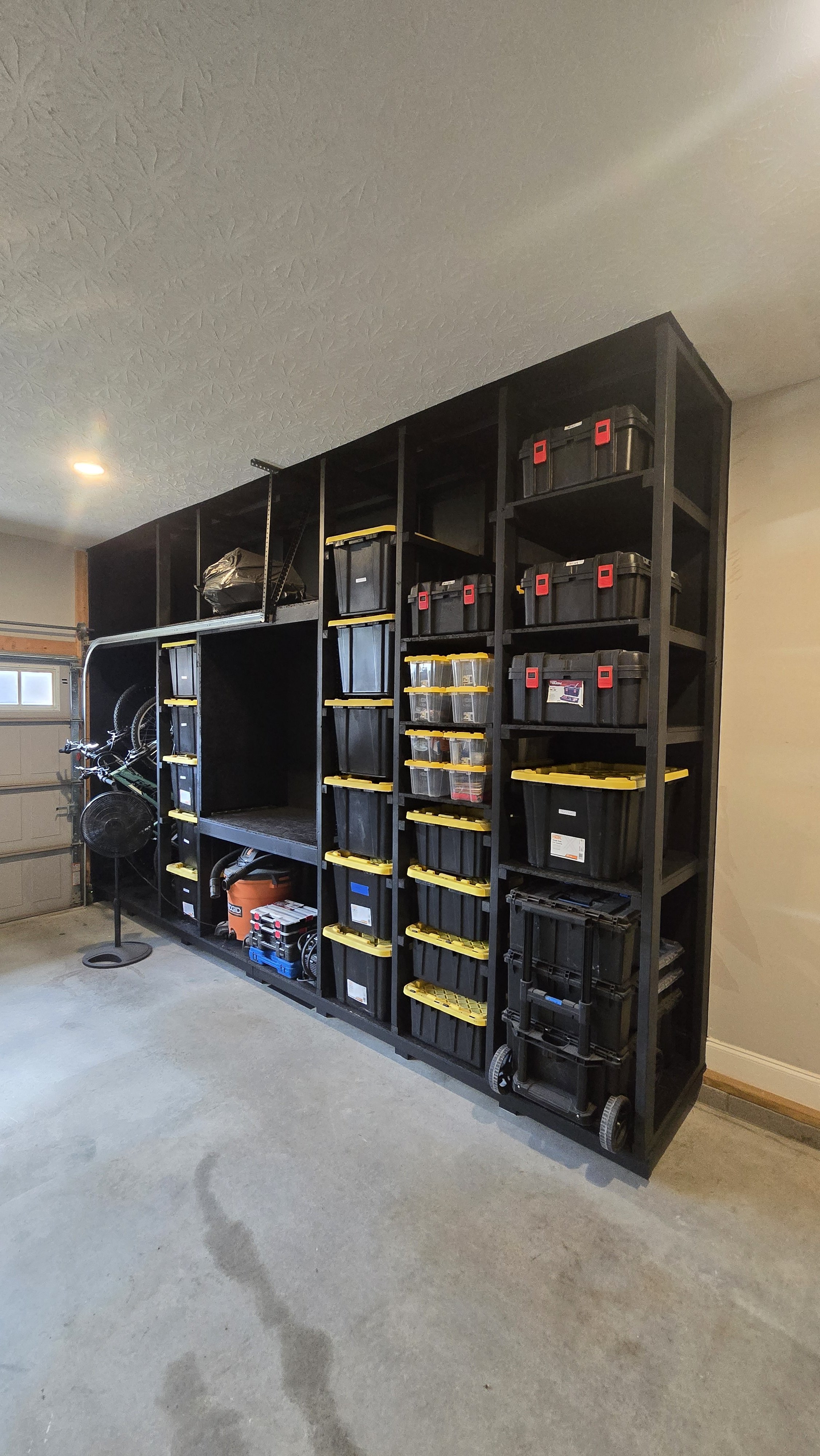 Garage with organized black storage shelves filled with plastic bins, tools, and equipment, beside a closed garage door.