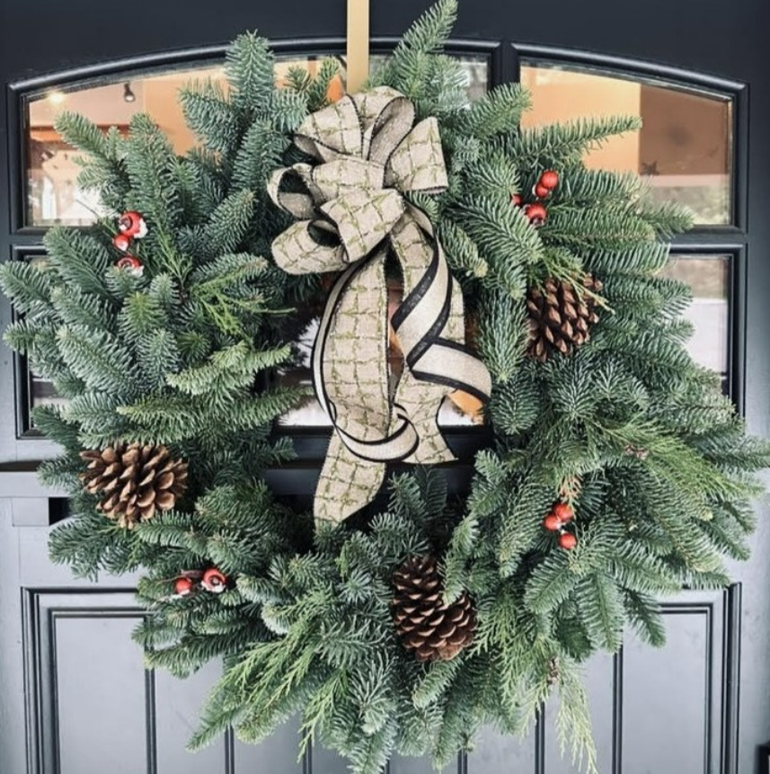 Christmas wreath made of pine branches with pinecones, red berries, and a large decorative bow hanging on a door.