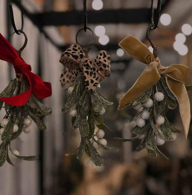 Decorative holiday ornaments with faux greenery, frosted berries, and fabric bows in red, leopard print, and gold, hanging from hooks.