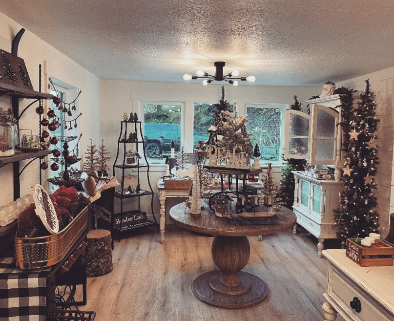 A holiday decorated living room with Christmas trees, ornaments, and a table centerpiece, featuring a white cabinet and a large window with a vehicle outside.