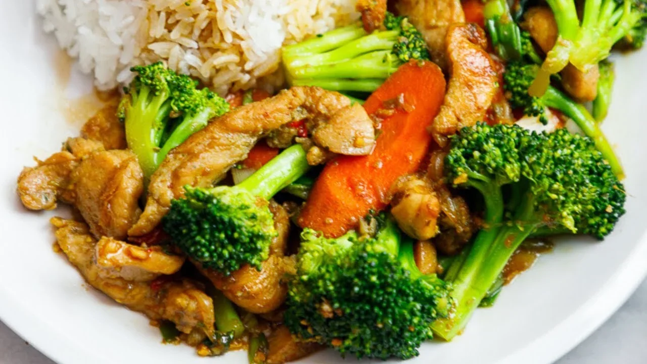 A plate of stir-fried broccoli, carrots, and chicken served with rice.