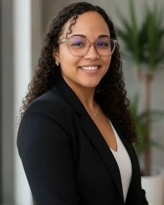 Professional woman with curly hair and glasses smiling indoors.