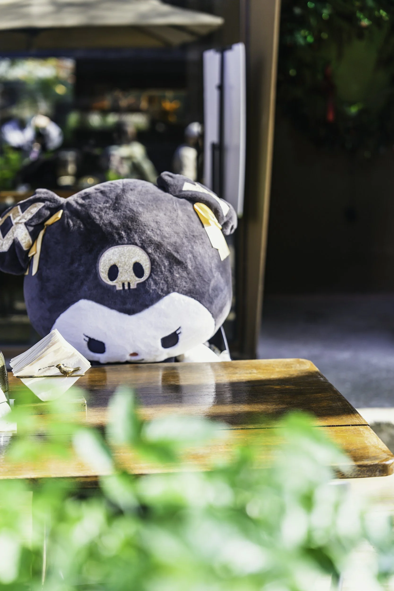 Gray skull-themed plush toy sitting at a wooden café table