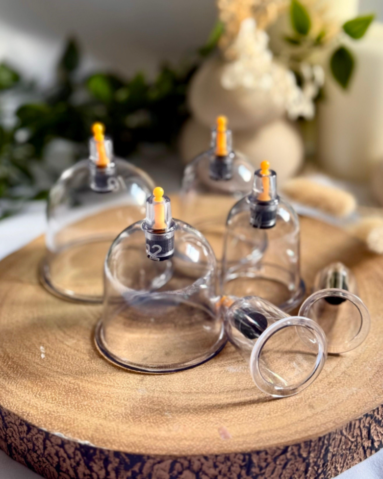 Four glass cupping therapy cups with orange valves on a wooden round tray