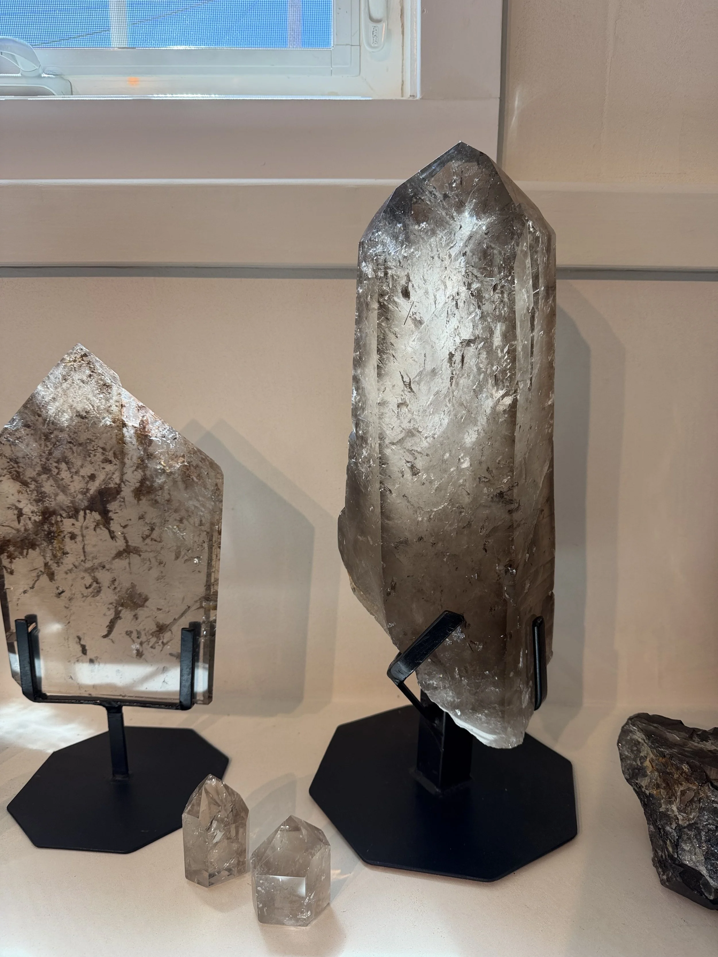 Various large crystal mineral specimens displayed on black stands in a room, with a window and a white wall in the background.