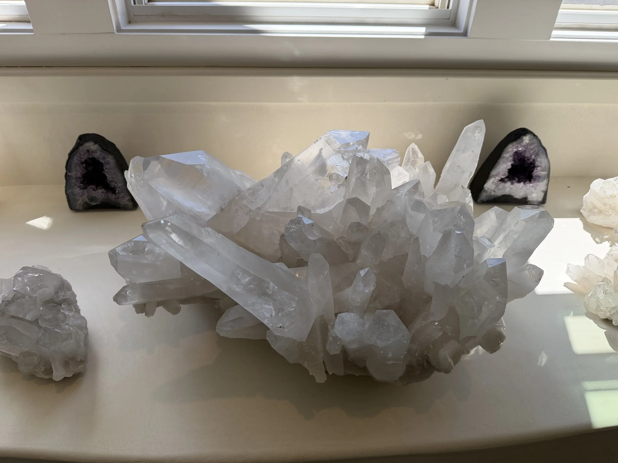 A collection of geodes with dark outer shells and purple and white crystalline interiors, positioned on a windowsill.