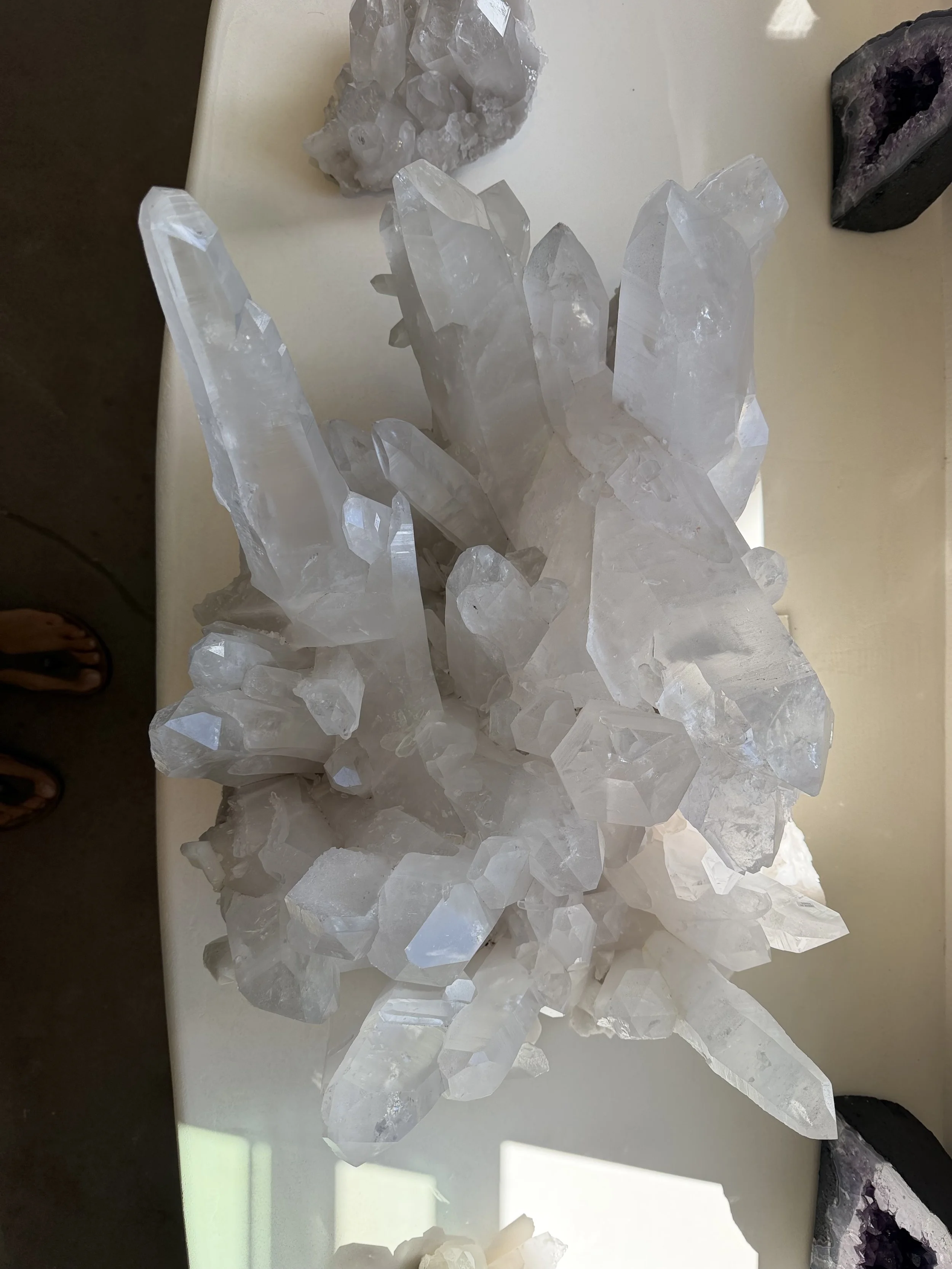Various quartz crystals on a white surface, including clear quartz points and amethyst geodes.