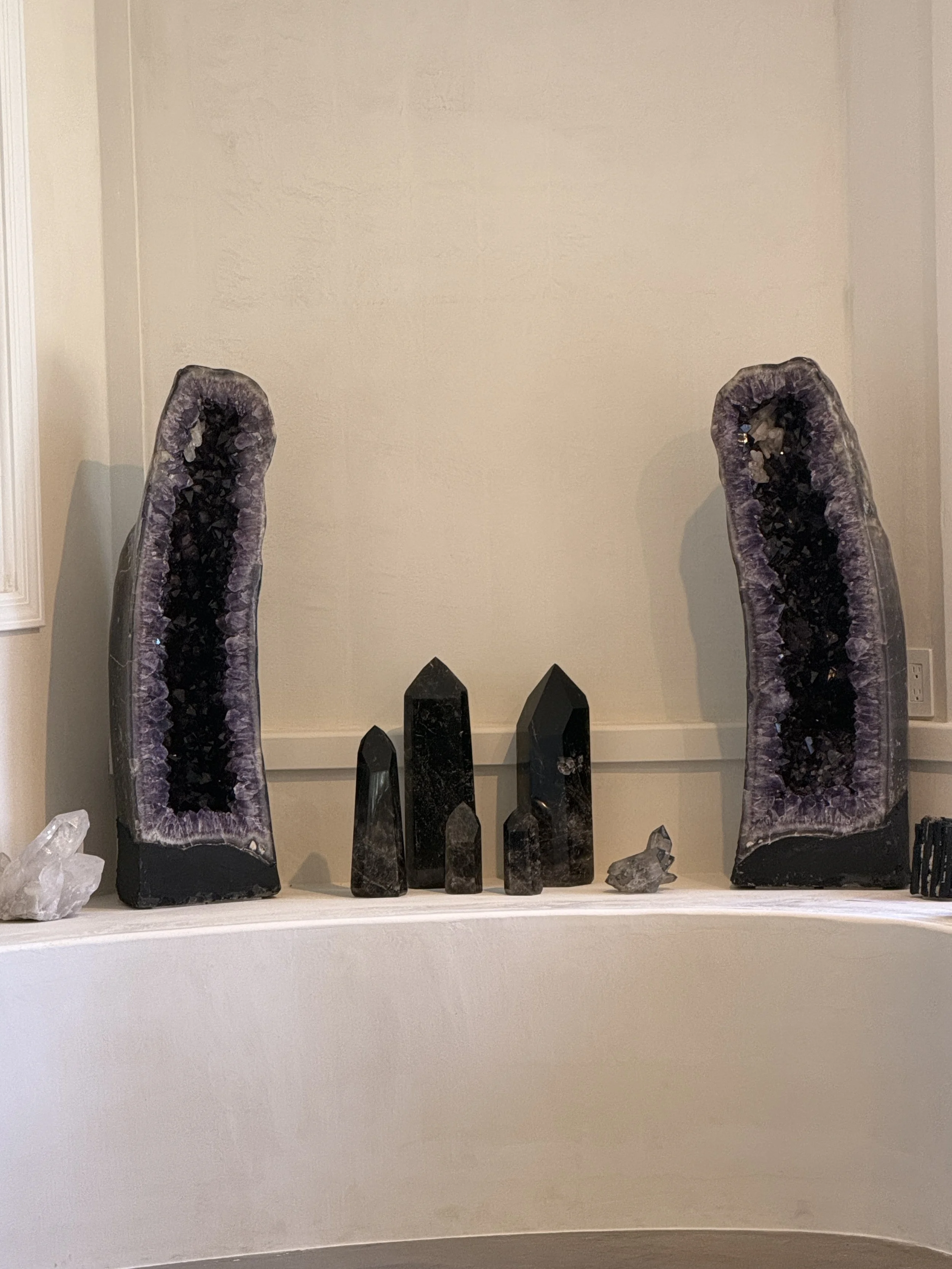 Decorative display of several large amethyst geodes and smaller crystal minerals on a white shelf against a beige wall.