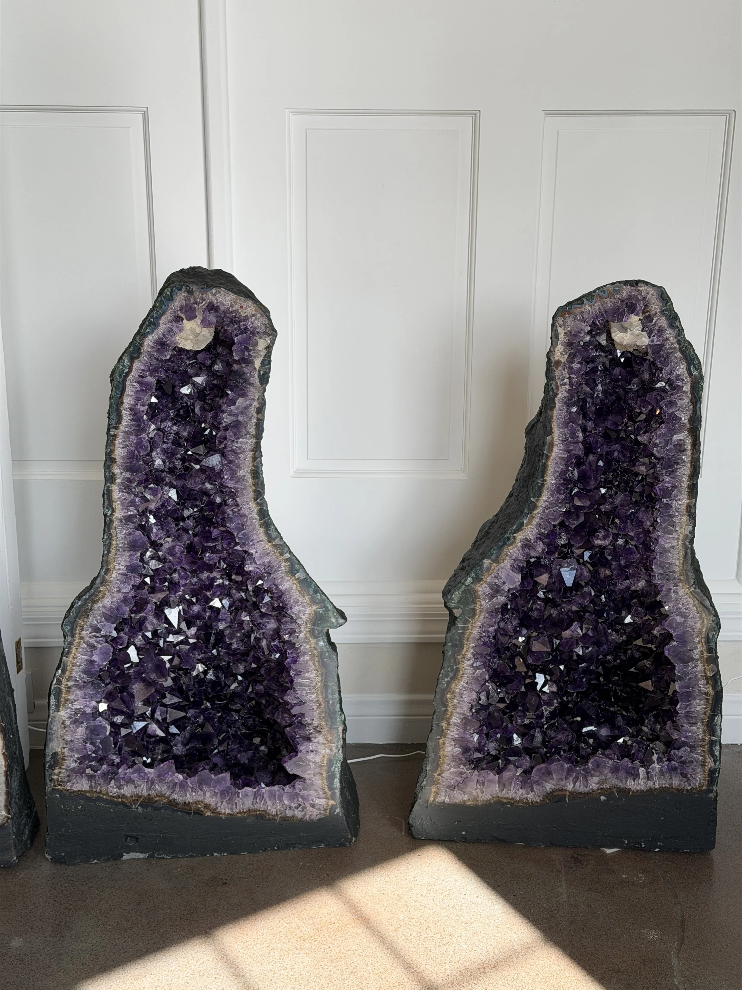 Two large amethyst geode sculptures standing upright against a white wall.