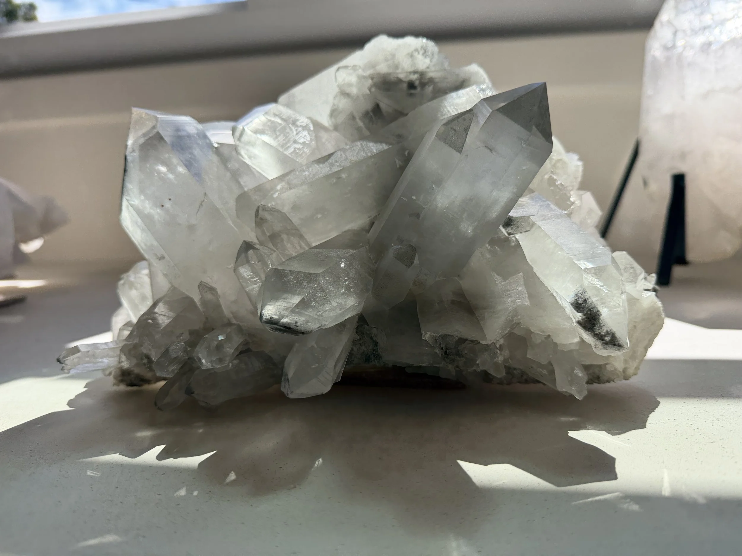 Close-up view of a cluster of clear quartz crystals with sunlight casting shadows on a white surface.