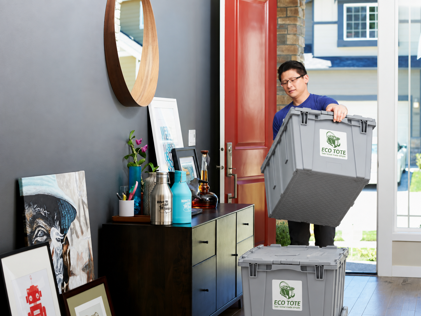 A man lifting a gray eco-friendly storage container labeled 'ECO TOTE' into a house through the front door.
