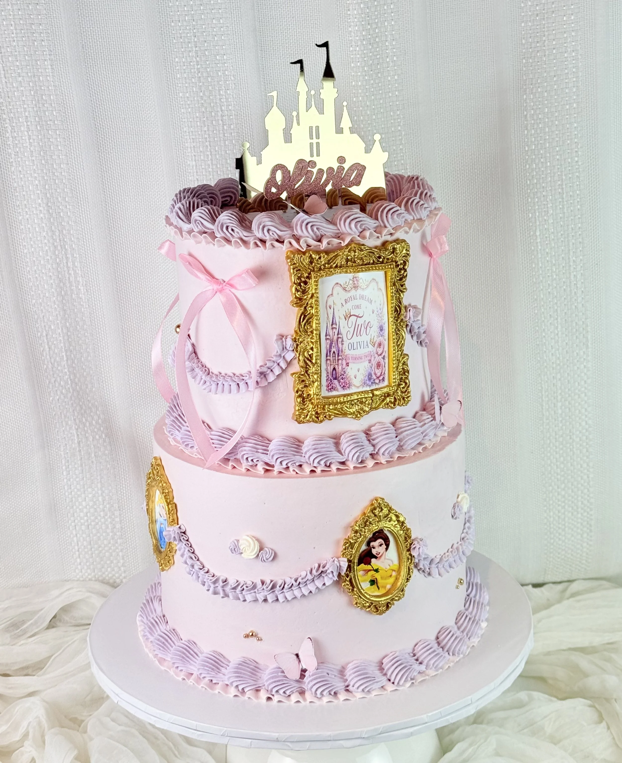 A three-tier pink castle-themed birthday cake decorated with purple/white swirls, gold frames with princess images, pink ribbons, and a princess castle topper with the name 'Olivia'.