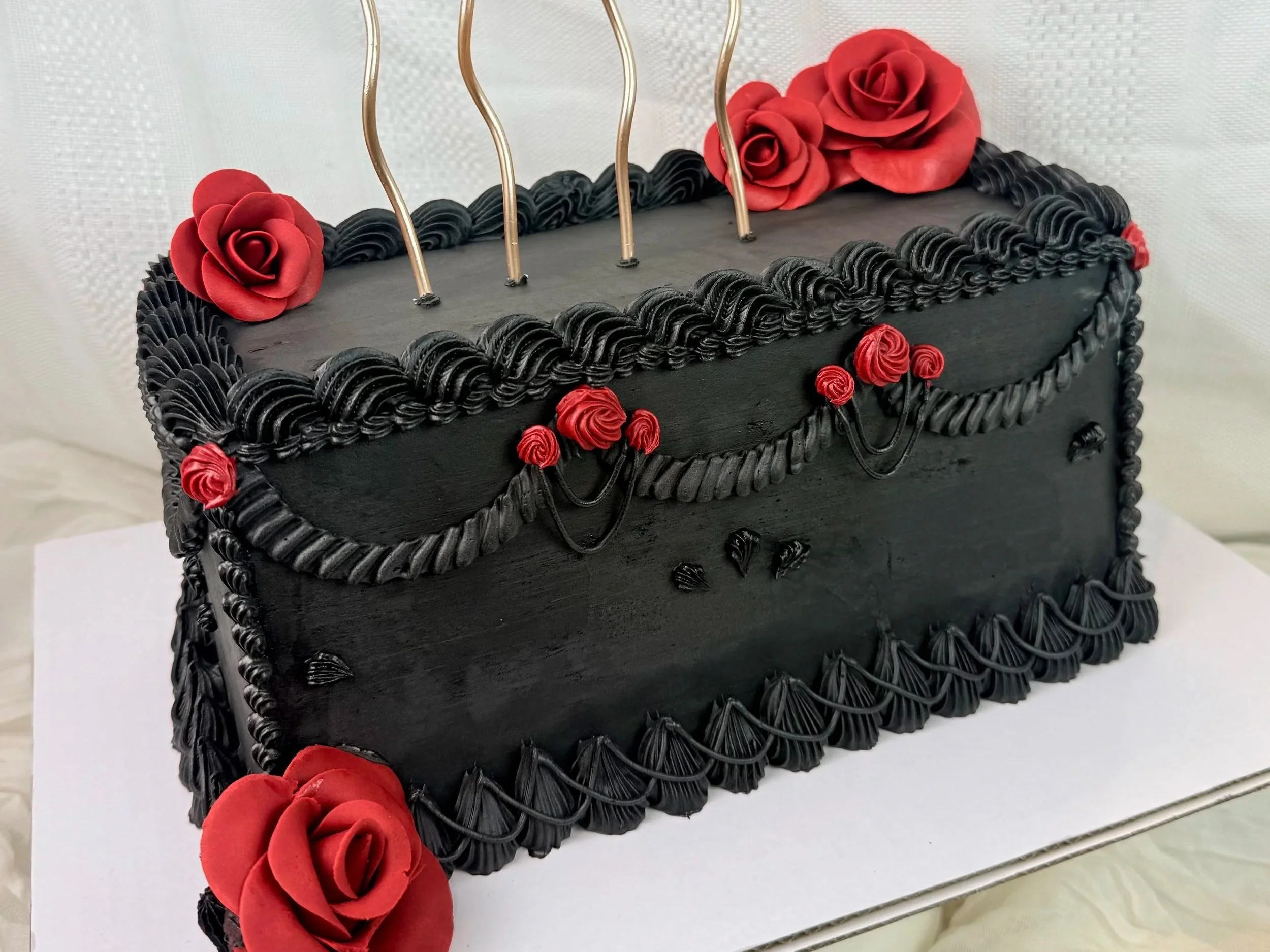 A rectangular black cake decorated with black icing and red roses made of fondant or icing on top, sides, and corners.