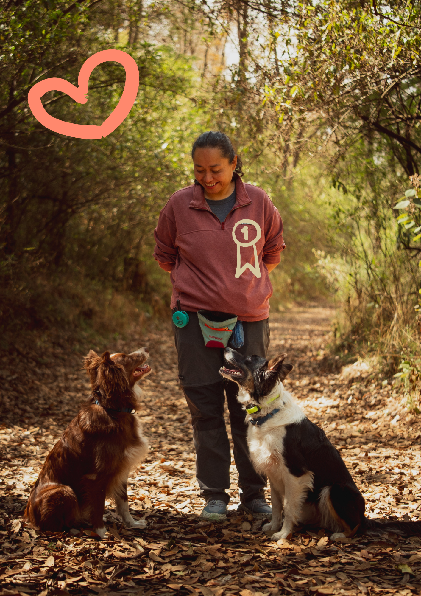 Mujer sonriente en el sendero del bosque con dos perros, uno de raza Border Collie y otro de raza Retriever, con un fondo de árboles con hojas secas en el suelo y un dibujo de corazón naranja en la esquina superior izquierda.